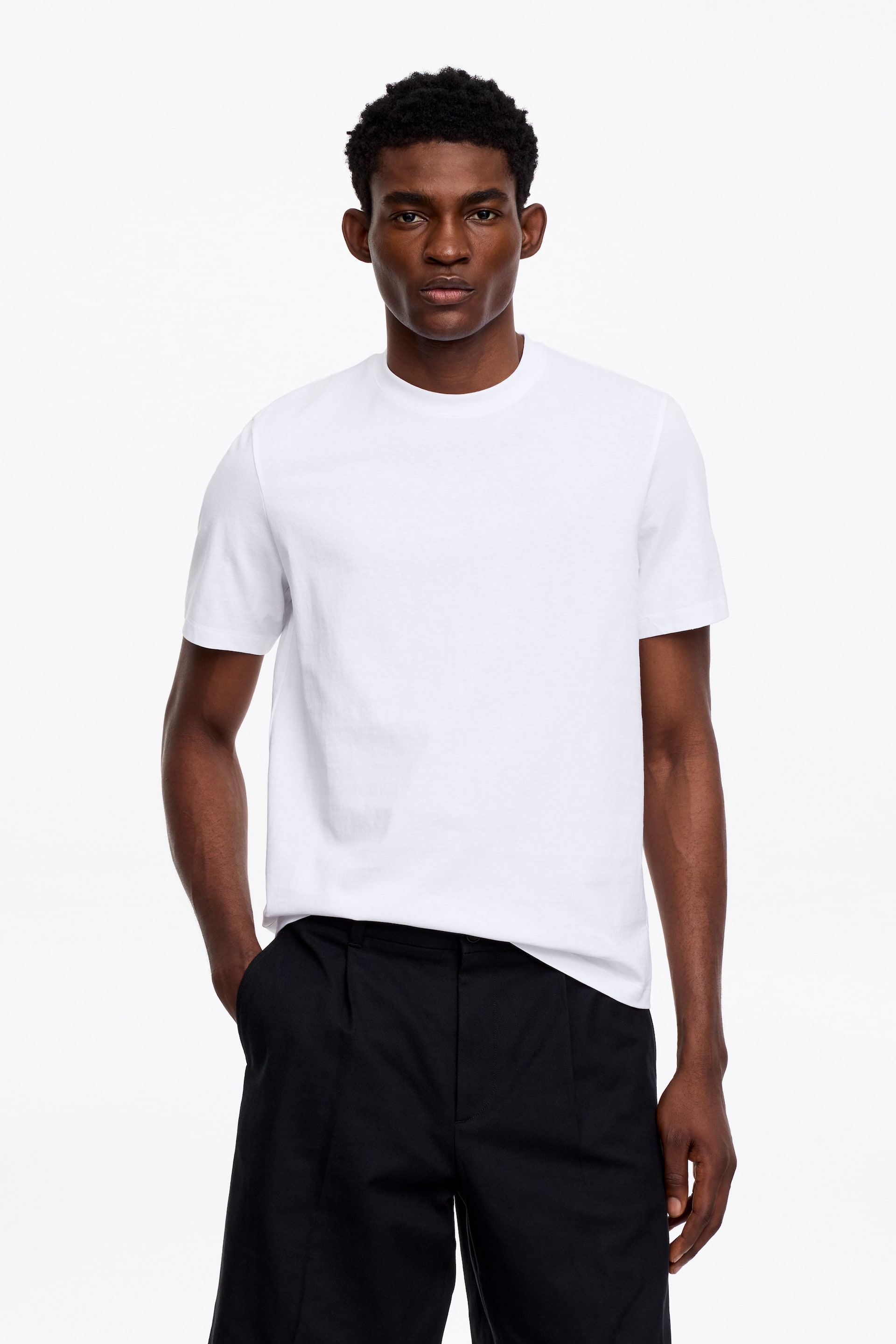 Agrandir l'image: Un t-shirt blanc est porté, affichant un col rond, des manches courtes et une coupe décontractée.