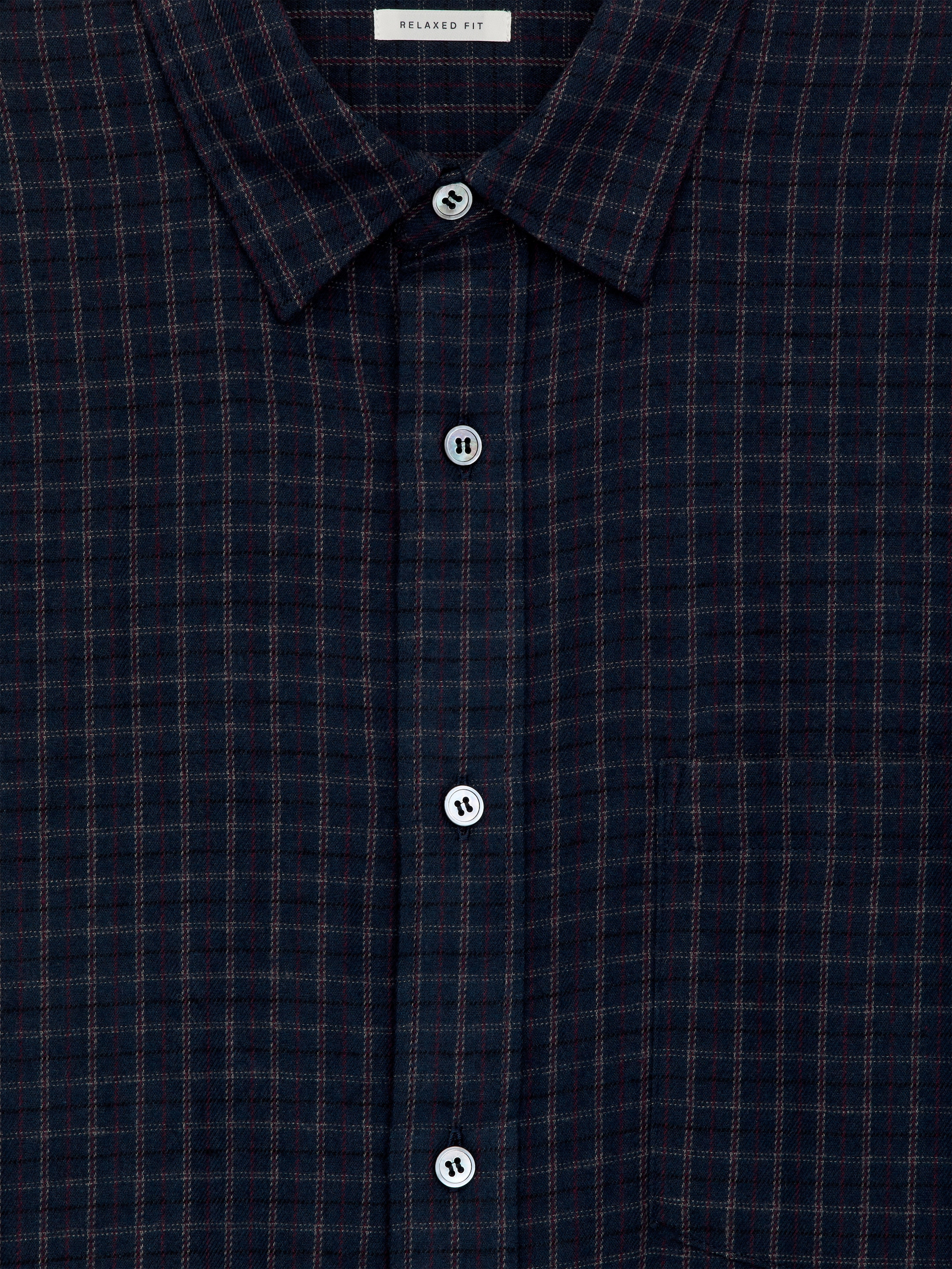 Visualizza immagine più grande: Una camicia di flanella di cotone è esposta dalla parte anteriore, caratterizzata da un colore blu scuro con un sottile motivo a quadri rosso. Include una singola tasca sul petto ed è chiusa con bottoni in madreperla bianca lungo l'abbottonatura anteriore, con un'etichetta 'RELAXED FIT' visibile in alto.