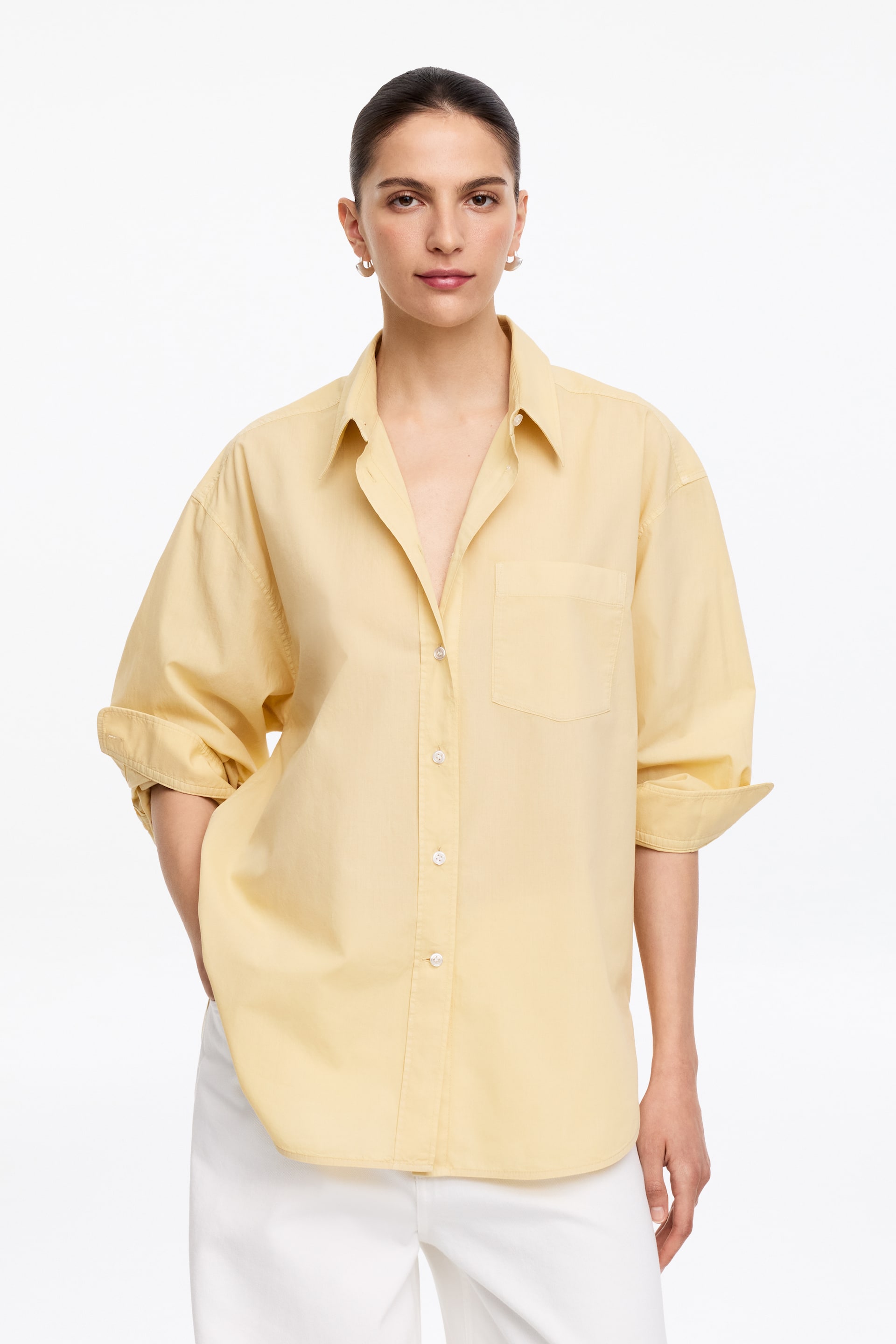 Agrandir l'image: La chemise jaune est orientée vers l'avant, avec un col pointu, une fermeture à boutons sur le devant avec des boutons blancs, et une poche plaquée unique sur la poitrine gauche. Elle présente une coupe décontractée et ample, avec ses manches longues retroussées jusqu'aux avant-bras.