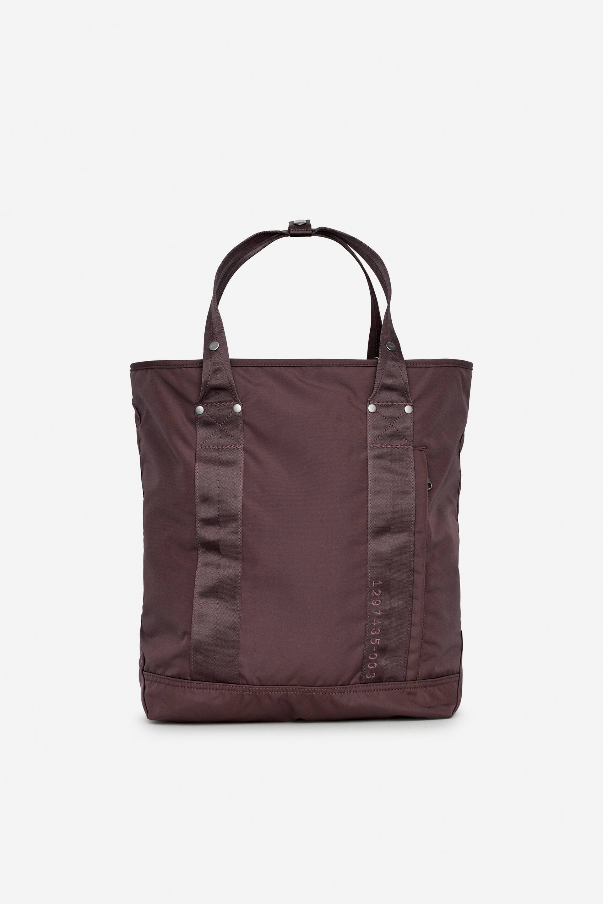 Преглед на по-голямо изображение: Тъмно лилава платнена чанта с лице напред, с две горни дръжки, съединени с малък метален закопчалка. Два вертикални ремъка от лента минават по предната част, закрепени със сребристи нитове, с надпис "1297435-003", отпечатан вертикално на десния ремък.