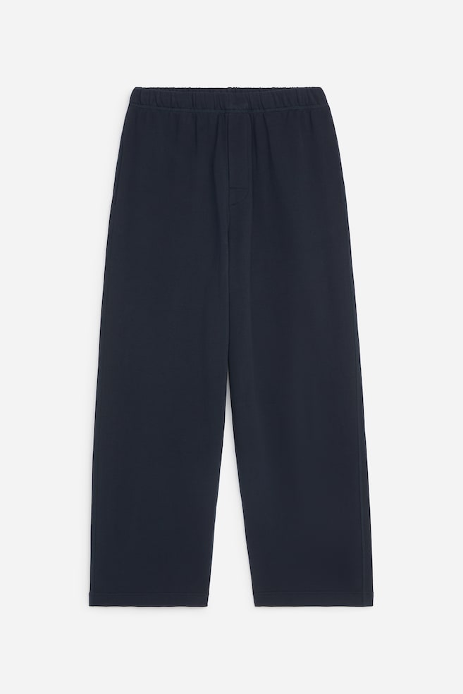 Se muestra un par de pantalones azul marino de pierna ancha, vistos de frente, con una cintura elástica fruncida y un discreto detalle de pespunte simulando bragueta. El estilo de corte holgado presenta perneras rectas con bajos de acabado limpio y bolsillos en las costuras laterales. - 1