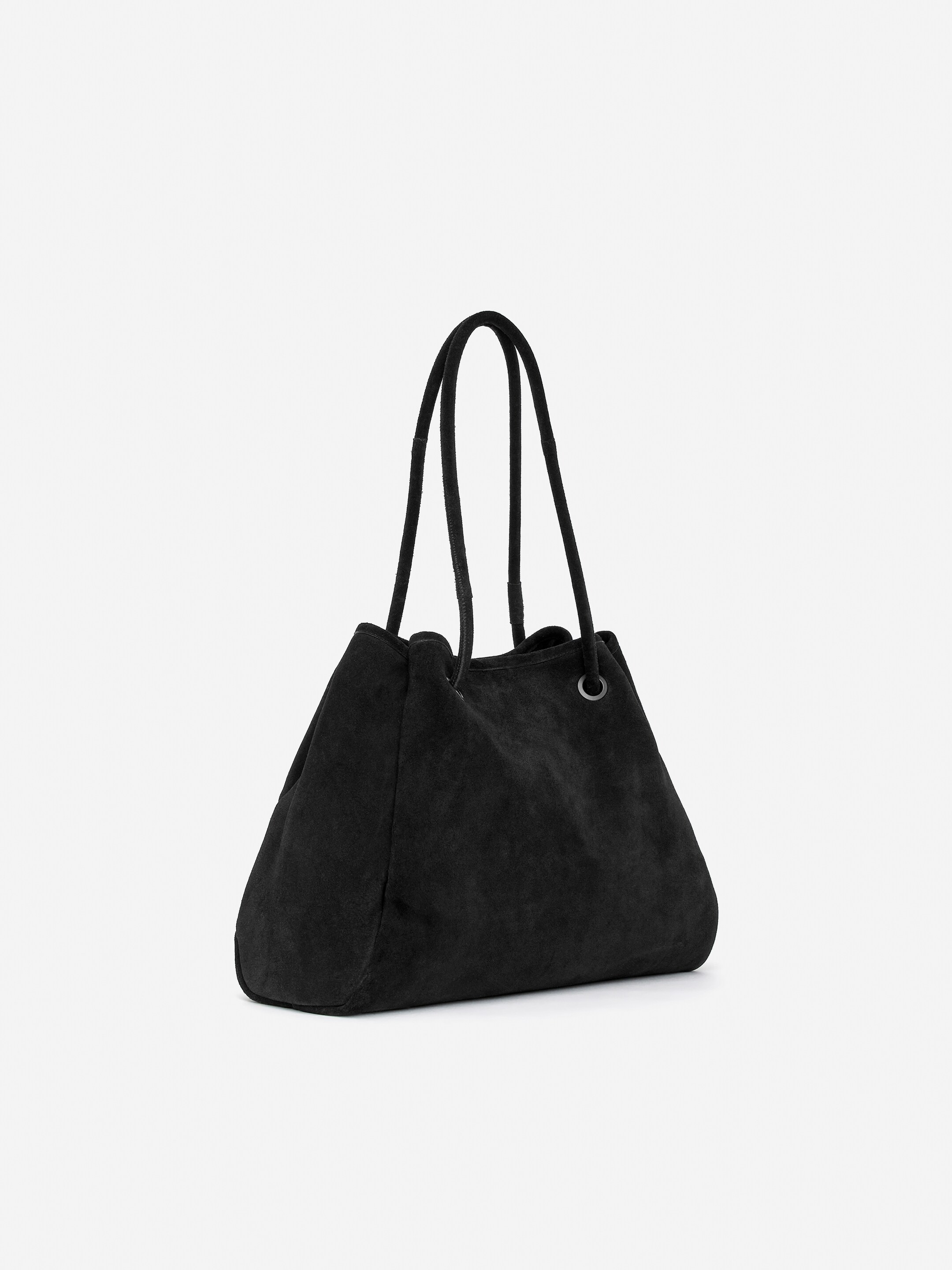 Agrandir l'image: Un sac fourre-tout en daim noir est présenté incliné vers la gauche, avec une structure souple et décontractée. Ses bretelles tubulaires glissent à travers des œillets, resserrant l'ouverture supérieure du sac.