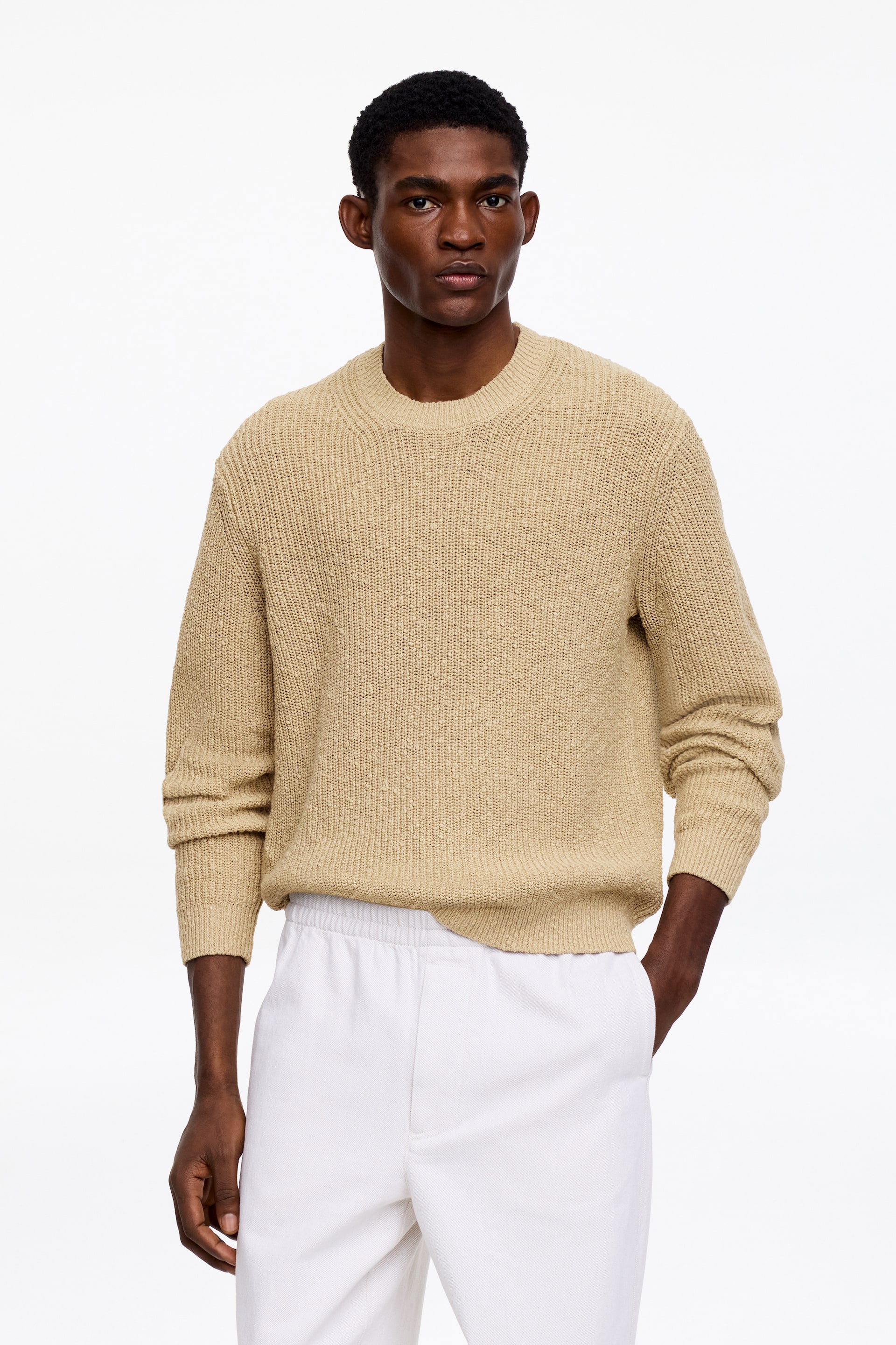 Visa större bild: En beige tröja med rund hals, långa ärmar och ribbade muddar och fåll. Den visar ett texturerat stickmönster och en avslappnad passform.