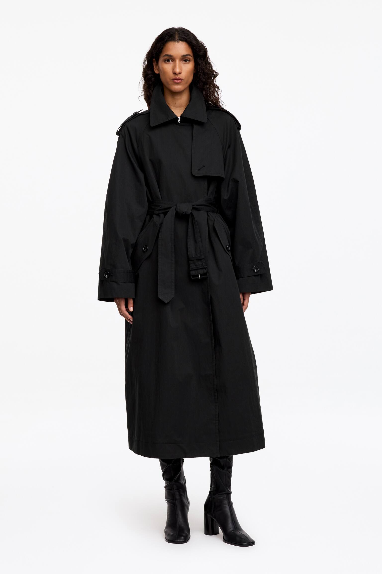 A modell egy fekete, oversized trench kabÃ¡tot visel, szÃ©les hegyes gallÃ©rral, vÃ¡llpÃ¡ntokkal, viharlappal Ã©s Ã¡llÃ­thatÃ³ mandzsettapÃ¡ntokkal. A kabÃ¡tot a derÃ©knÃ¡l az anyagÃ¡val megegyezÅ Ã¶v fogja Ã¶ssze, Ã©s fekete, magassarkÃº csizmÃ¡val pÃ¡rosÃ­tja. - 1