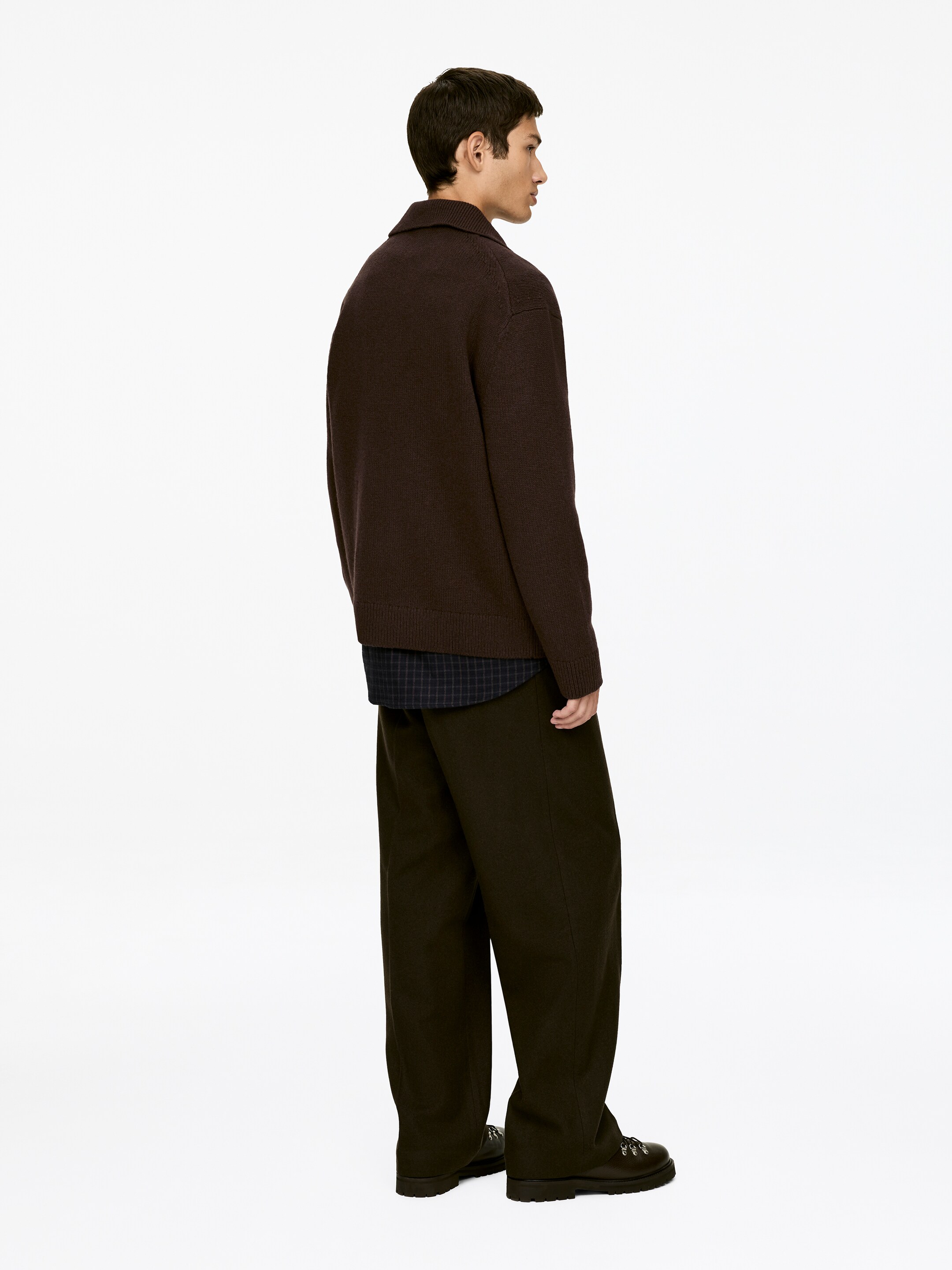 Agrandir l'image: Un polo en maille marron foncé, avec un col évasé et des manches longues, est porté. Il est superposé à une chemise à carreaux foncés et associé à un pantalon large marron foncé et des bottines à lacets foncées, le tout présenté de côté.