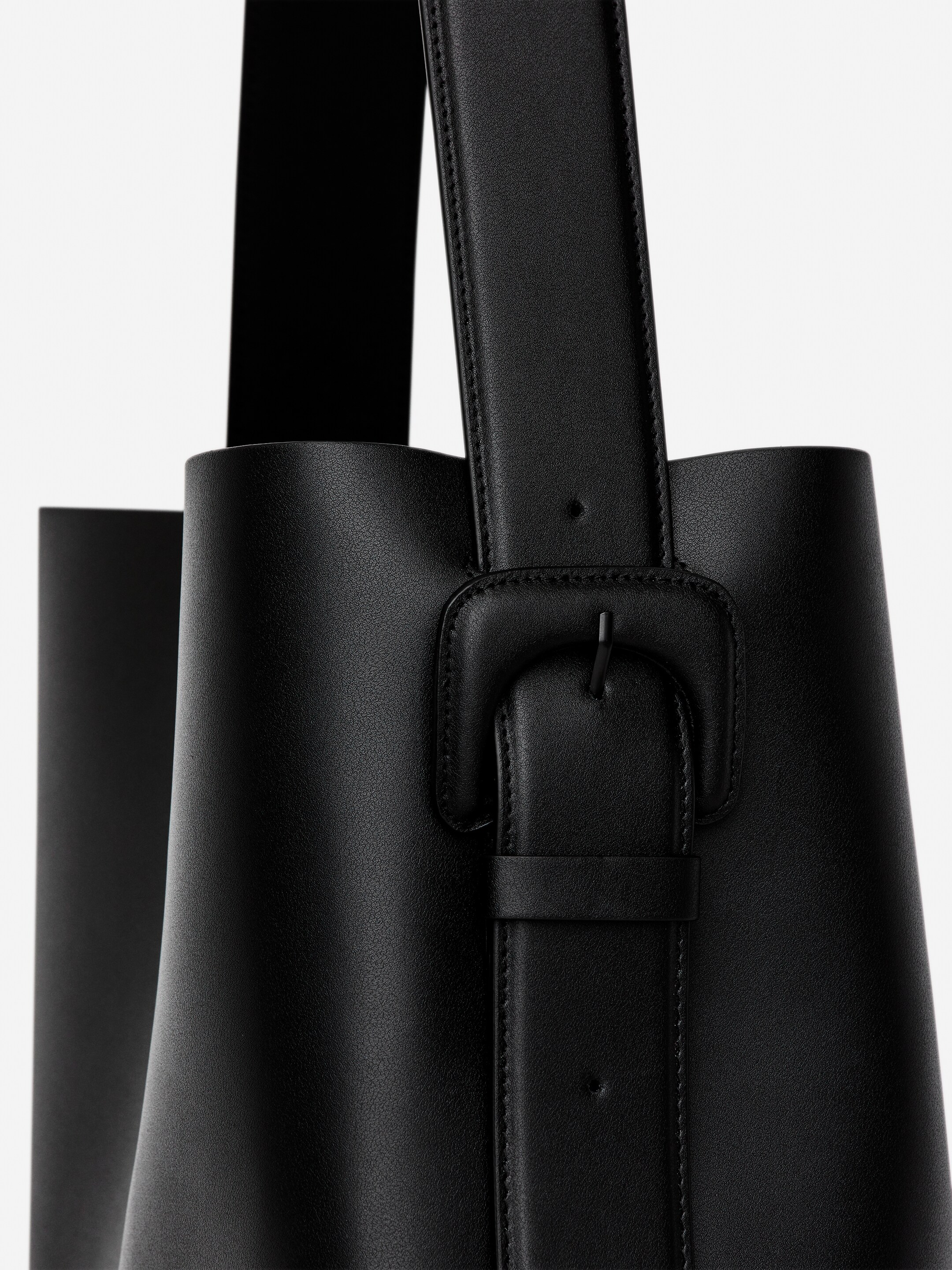 Größeres Bild anzeigen: Eine schwarze Tragetasche wird präsentiert, die ein strukturiertes Design aufweist. Ein schwarzer verstellbarer Riemen ist mit der Tasche über eine rechteckige Schnalle mit einer Halteschlaufe verbunden, alles aus passendem Material mit sichtbaren Nähten.