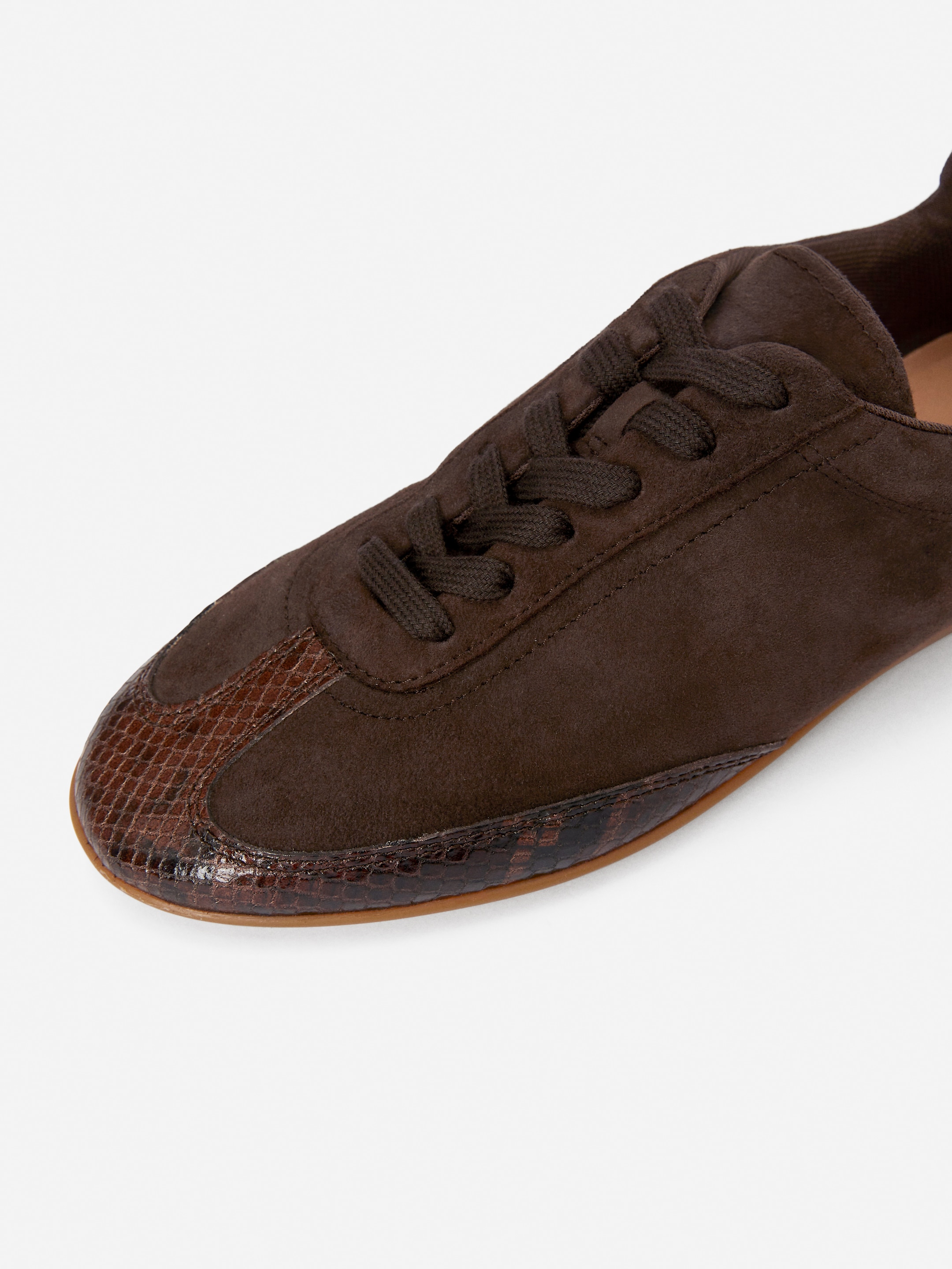 View larger image: A dark brown suede trainer is presented from a top-down angle, featuring a lace-up front. It is designed with a patterned, reptilian-embossed leather accent on the rounded toe cap and along the side of the shoe.