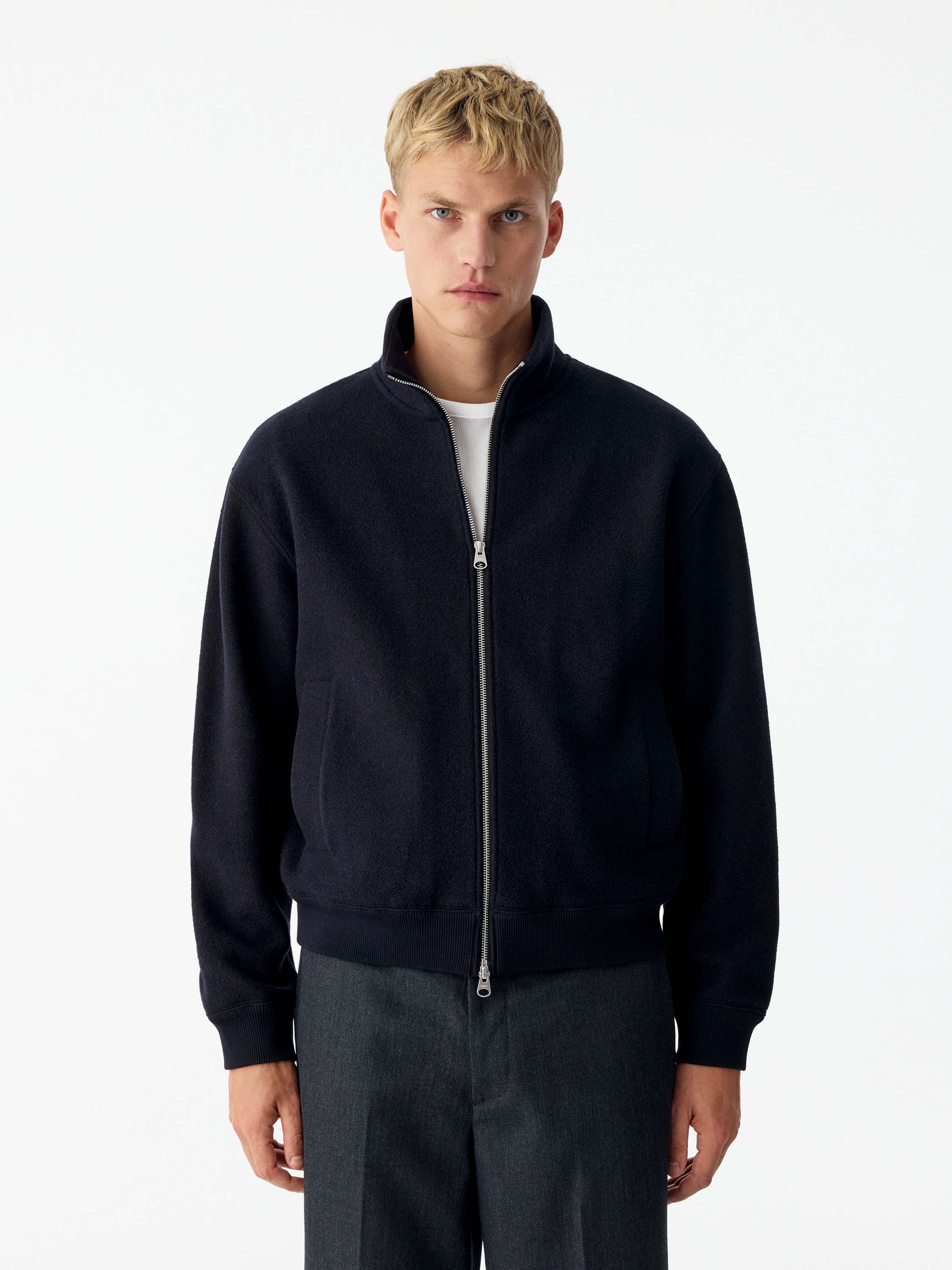 Una giacca zip-up blu navy scuro Ã¨ mostrata frontalmente, caratterizzata da una zip frontale color argento, un colletto alto rialzato e bordi a coste sui polsini e sullâorlo. La giacca presenta due tasche a filetto verticali sui lati e maniche lunghe con spalle leggermente scese.