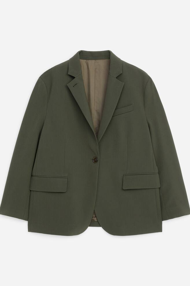 En olivengrÃ¸nn blazer er vist forfra, med jakkeslag med hakk, en enkel knappelukking og to klaffelommer foran. Den avslappede jakken har en brystlomme med kant pÃ¥ venstre side og et kontrasterende, lysere grÃ¸nt innerfÃ´r. - 1