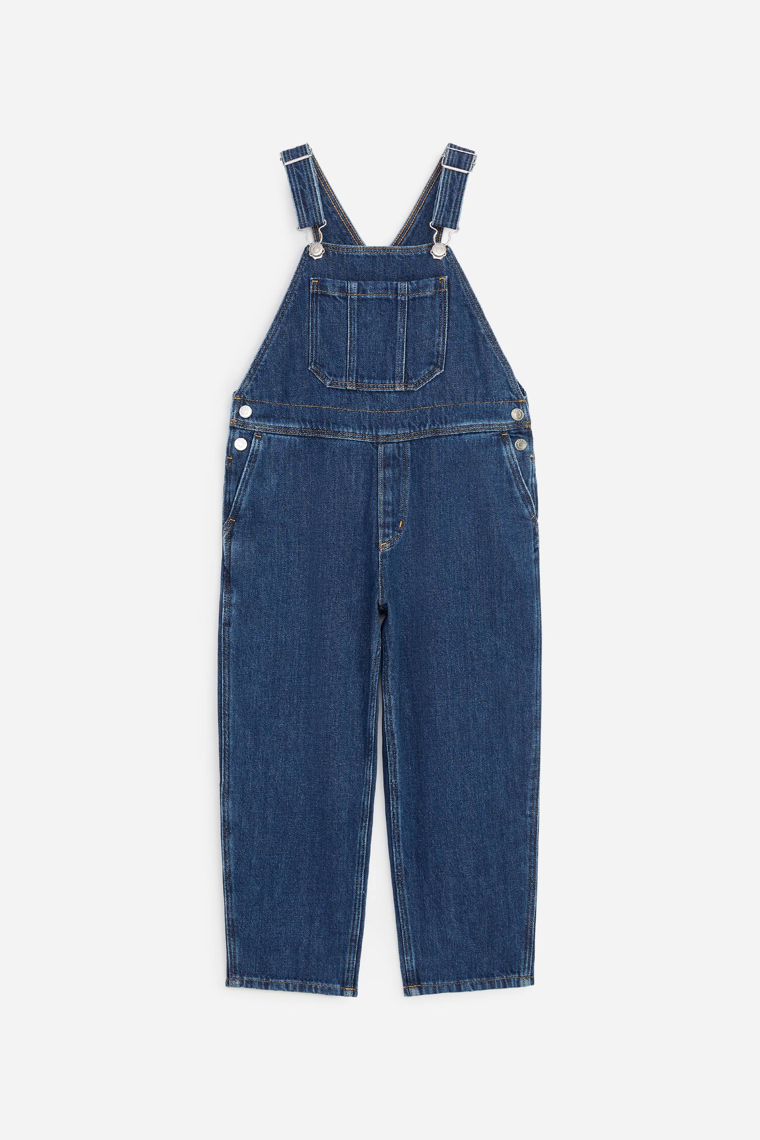 Ce salopette en denim prÃ©sente une silhouette Ã  jambes barrel vue de face. Le modÃ¨le est dotÃ© de bretelles rÃ©glables avec boucles mÃ©talliques argentÃ©es, dâune poche plaquÃ©e centrale sur la poitrine et de poches latÃ©rales en biais.