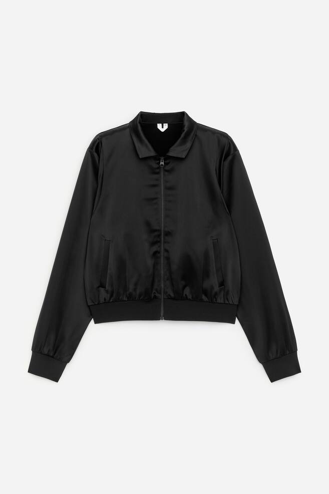 VORDERSEITE: Eine schwarze Bomberjacke zeigt einen dezenten Glanz, einen spitzen Kragen und einen durchgehenden Reißverschluss. Sie ist mit zwei Schlitztaschen sowie gerippten, elastischen Bündchen und einem passenden Saum ausgestattet. - 1