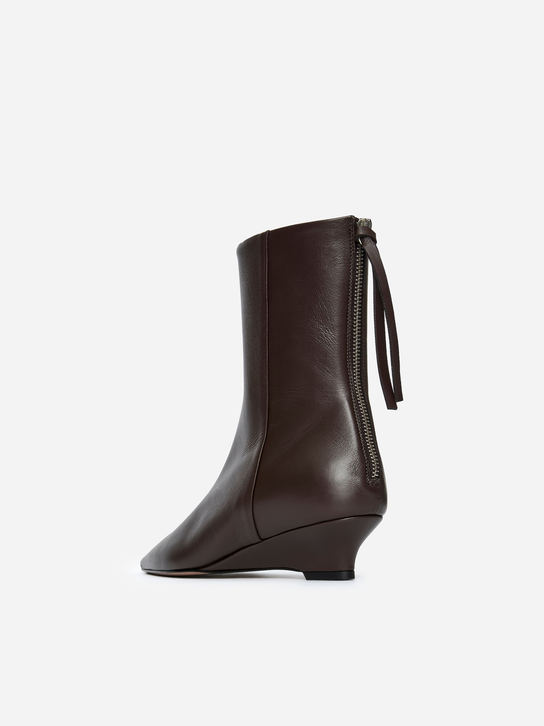 Se større billede: En mørkebrun læder ankelstøvle vender bagud, med en fuldlængde sølv lynlås, der løber ned ad skaftet med to hængende lædertrækstropper. Den fremviser en kilehæl og en diskret firkantet tå.