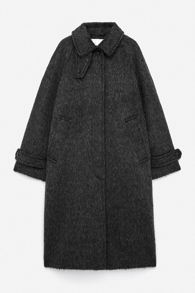 A dark grey single-breasted coat in a brushed wool and alpaca blend is presenting FRONT, featuring a rounded collar with a detachable storm flap. It is designed with raglan sleeves, buttoned tabs at the cuffs, a concealed button fastening down the front, and vertical welt pockets at the sides. - 1
