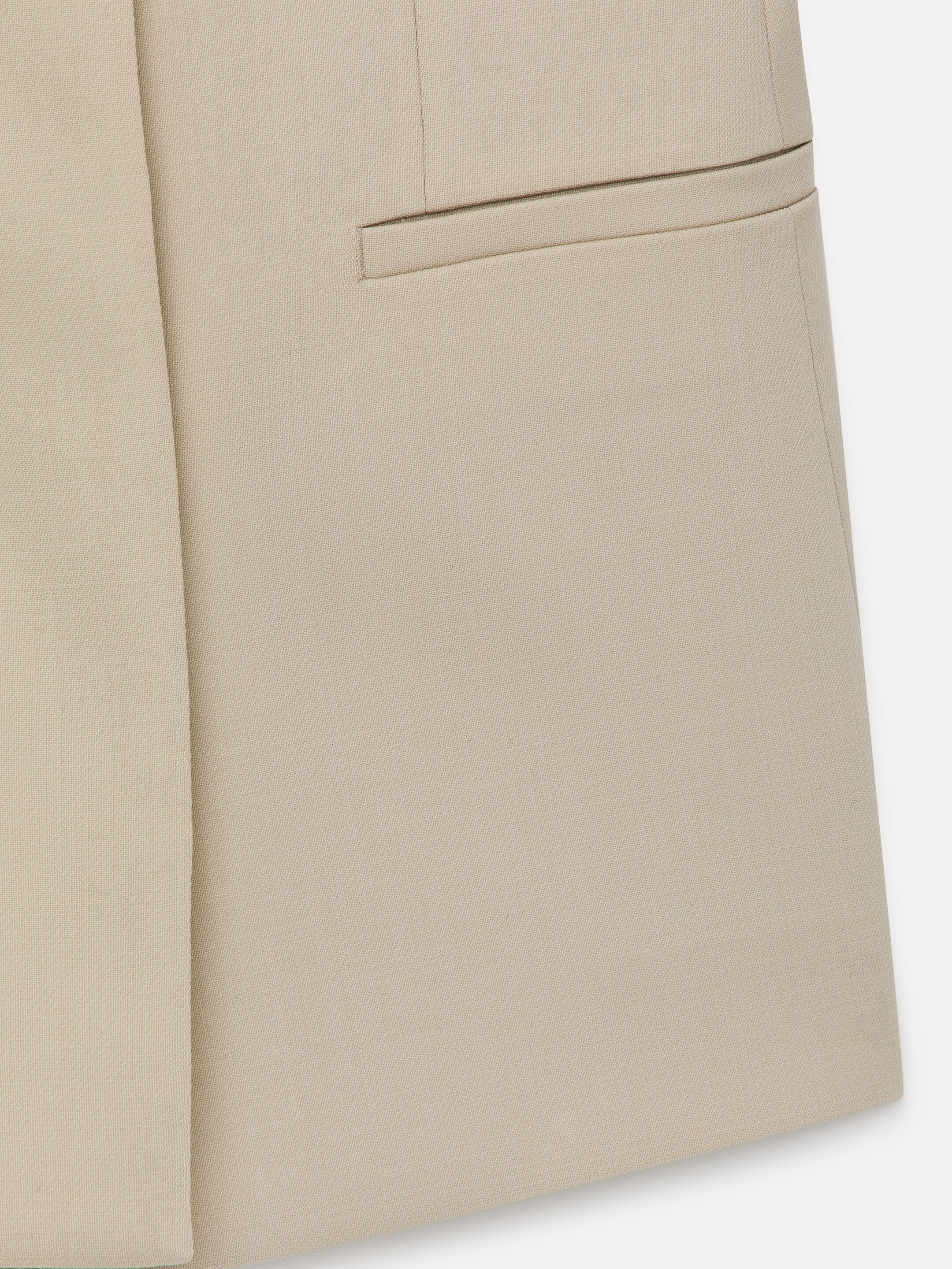 Agrandir l'image: Un vêtement ajusté de couleur beige clair présente une poche passepoilée horizontale sur le devant, avec une couture verticale à sa gauche.