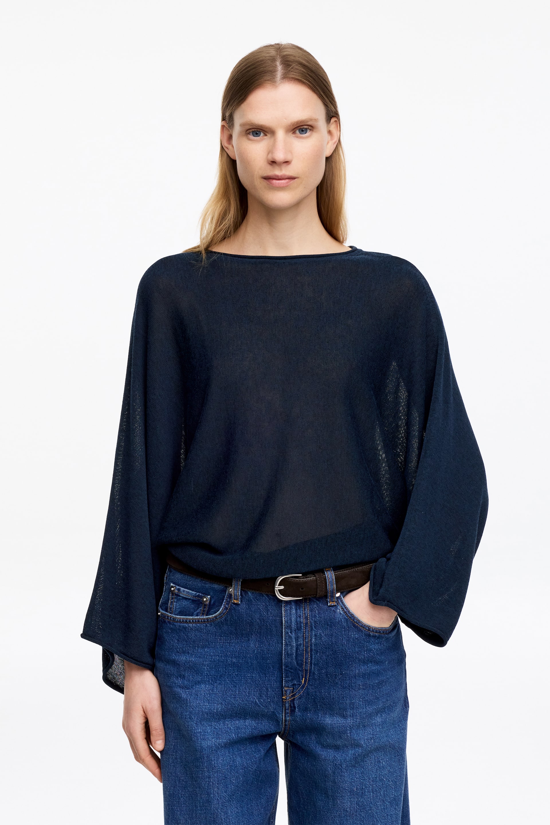 Agrandir l'image: Un haut en maille transparente bleu marine est présenté de face, avec une encolure bateau et des manches dolman. Le haut ample est porté rentré dans une ceinture, créant un drapé décontracté.