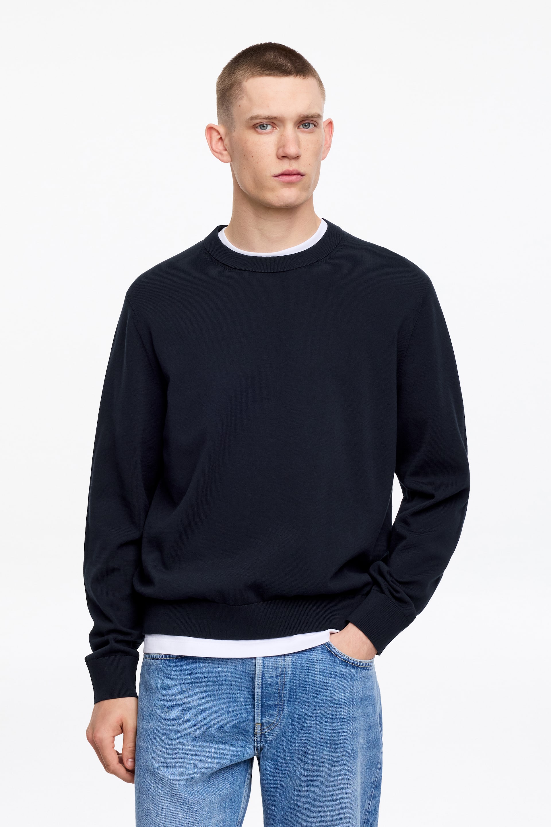 Visa större bild: Den marinblå crewneck-tröjan visar upp en ribbad crewneck, ribbade muddar och en ribbad fåll, och är vänd framåt. Den är lager på lager över en vit t-shirt, som syns vid halsringningen och under tröjans fåll.