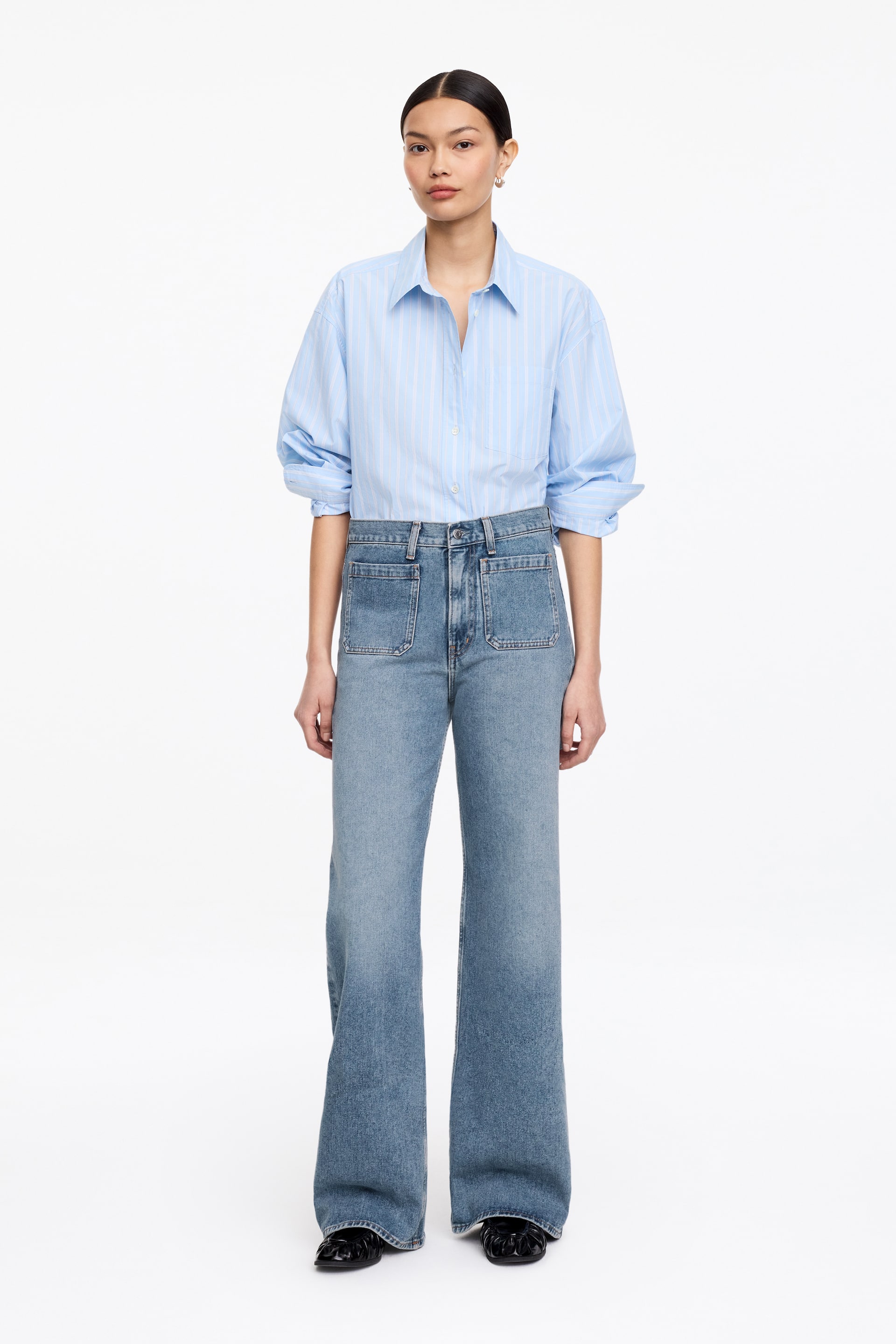 Größeres Bild ansehen: Die LUPINE-Jeans in einem hellblauen Stretch-Denim werden vom Model getragen. Sie zeichnen sich durch einen hohen Bund, eine schmale Passform am Oberschenkel, ausgestellte Beine und aufgesetzte Fronttaschen aus, mit einem Knopfverschluss am Hosenschlitz.