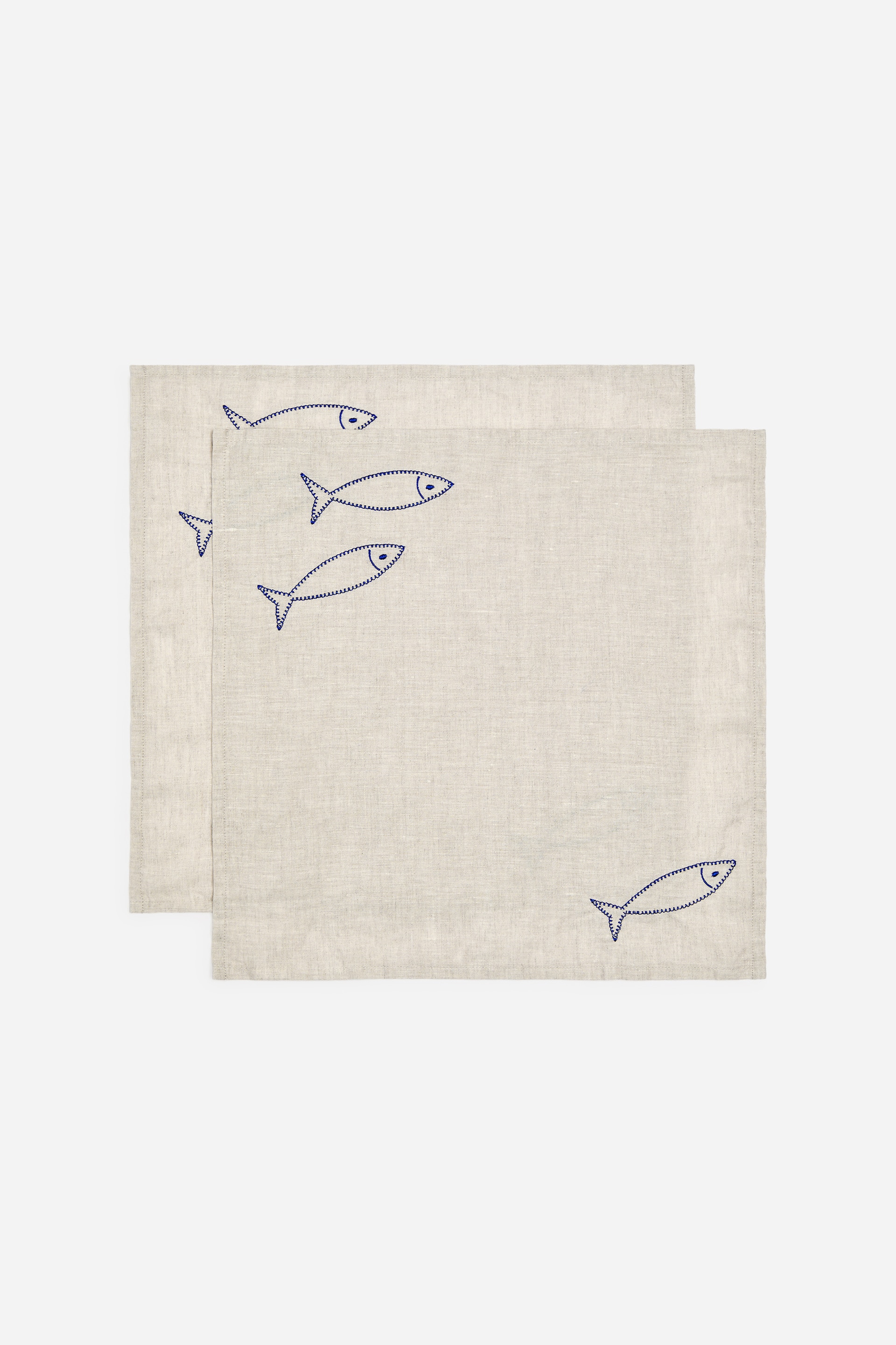 Agrandir l'image: Serviettes en lin brodées, lot de 2. Deux serviettes en lin beige clair sont superposées, l'une chevauchant légèrement l'autre. Chaque serviette présente des contours de poissons brodés en bleu, éparpillés.