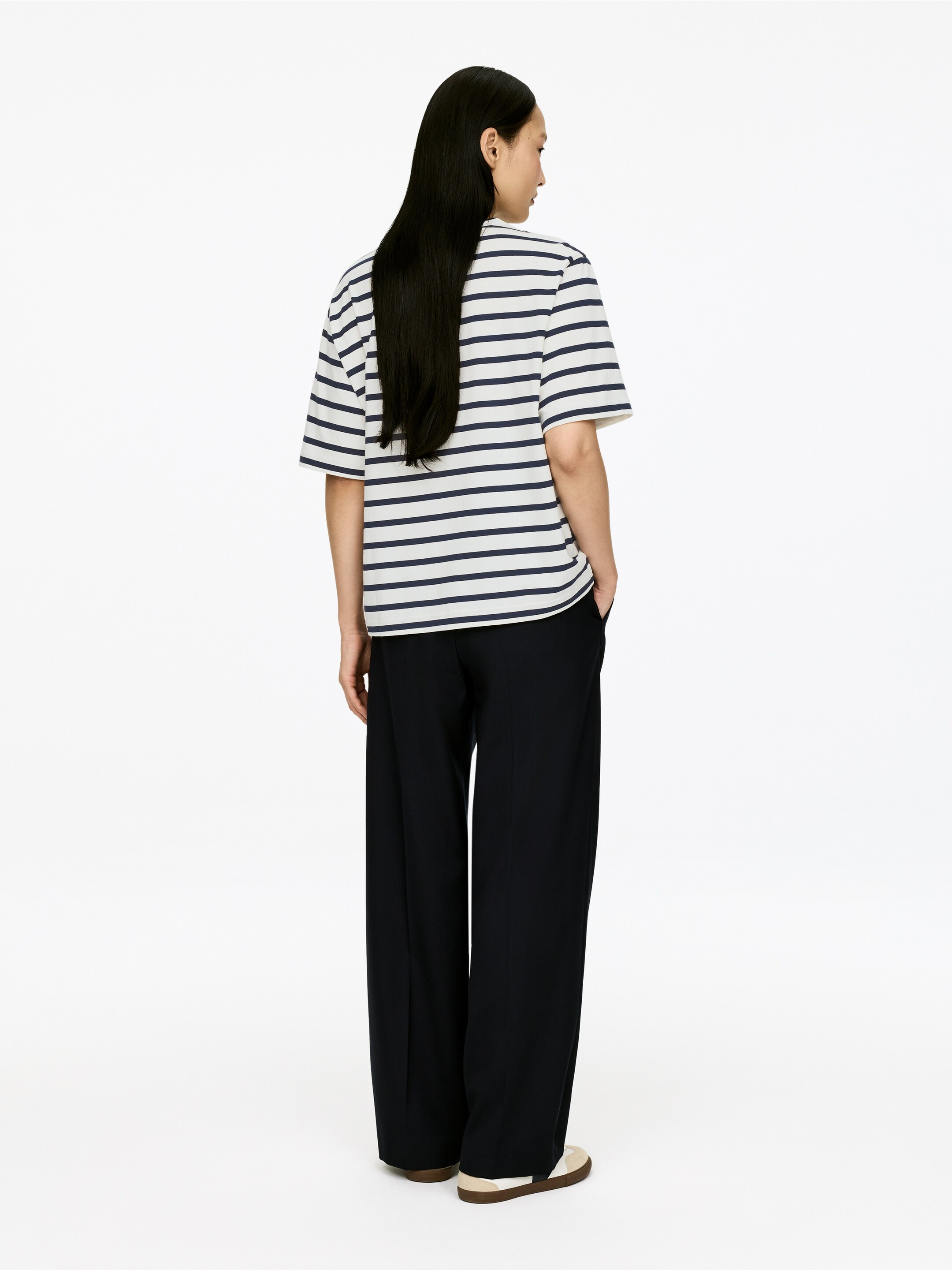 Agrandir l'image: Un t-shirt à manches courtes présente une base blanche avec des rayures horizontales bleu marine, présenté d'un angle arrière droit montrant sa coupe ample. Des pantalons noirs à jambes larges ont une coupe ample et s'étendent jusqu'au sol.