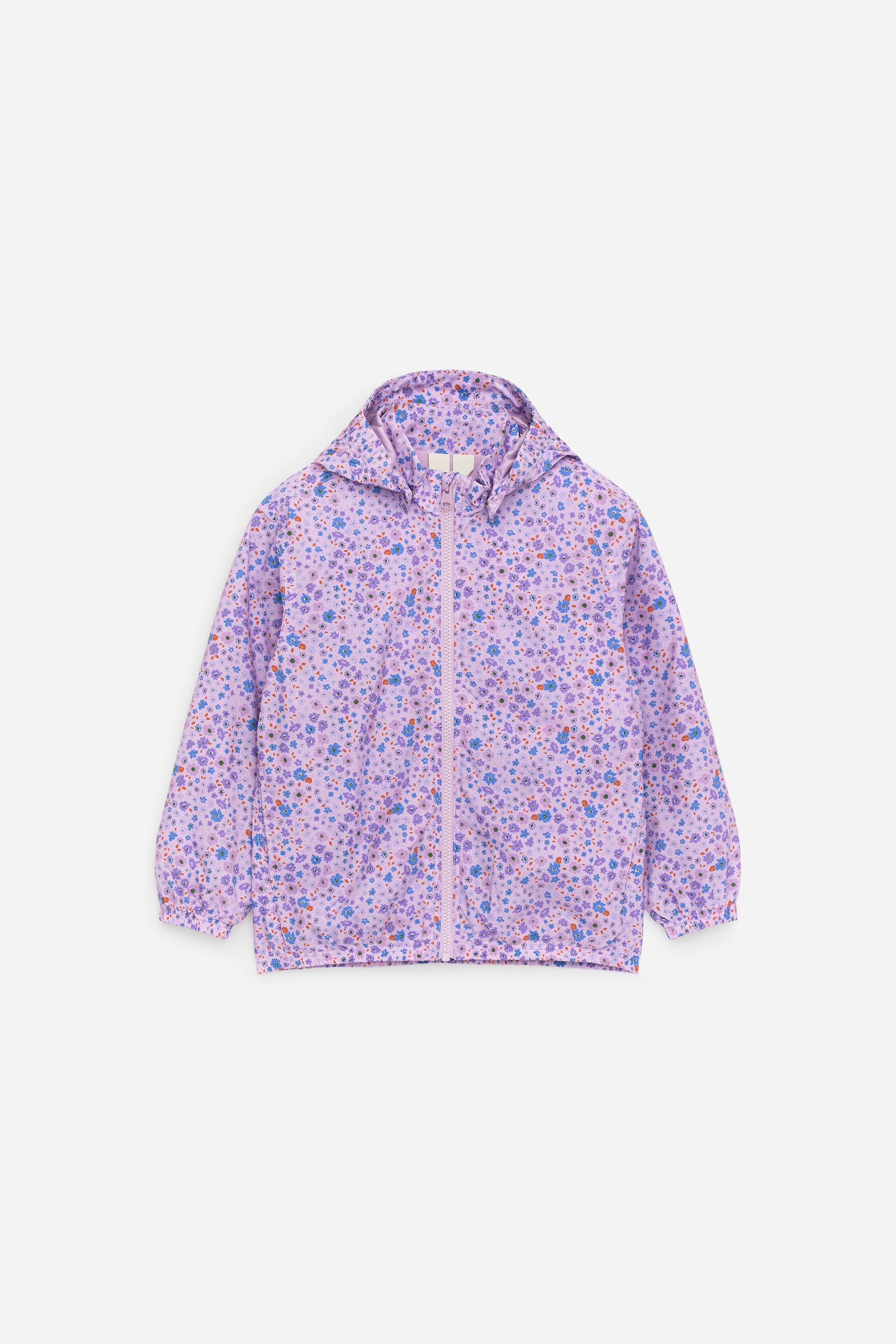 Visa större bild: Den ljuslila jackan är mönstrad med små blå, lila och orange blommor och prickar. Den har en huva, en dragkedja framtill och elastiska muddar och fåll.