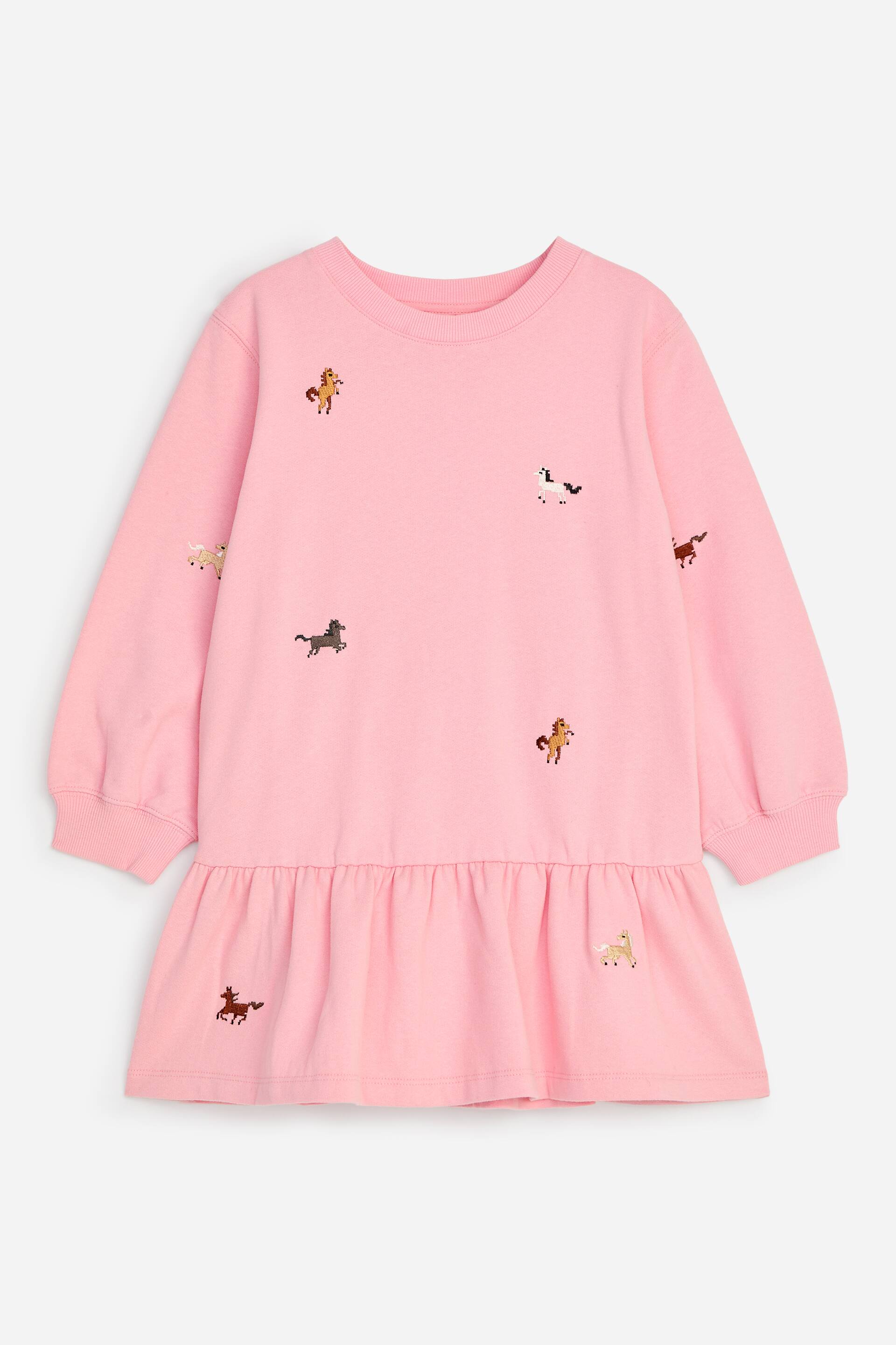 View larger image: A pink sweatshirt-style dress is shown from the front, featuring a relaxed fit with dropped shoulders, a ribbed crew neck, and ribbed cuffs. The dress is decorated with small, scattered embroidered horse motifs and features a gathered, ruffled skirt panel below the waist.