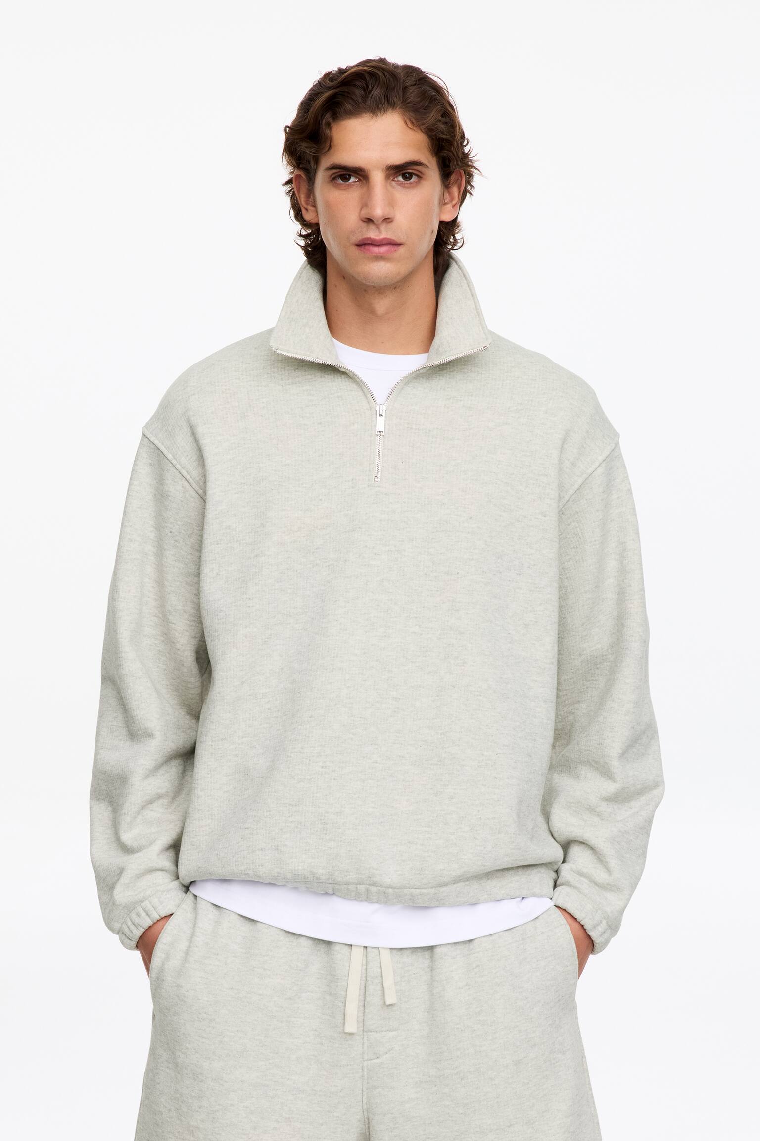 La modelo lleva una sudadera gris claro con media cremallera, cuello alzado, hombros caÃ­dos y puÃ±os y bajo elÃ¡sticos. La sudadera se lleva sobre una camiseta blanca y se combina con unos shorts de estar por casa a juego en gris claro. - 1