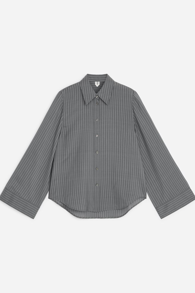 Eine graue Bluse mit feinen Nadelstreifen ist von vorne zu sehen und verfügt über einen spitzen Kragen, eine durchgehende Knopfleiste und einen abgerundeten Saum. Die langen Ãrmel weiten sich zu den Handgelenken hin und enden in breiten, geknöpften Manschetten mit horizontalen Streifendetails. - 1