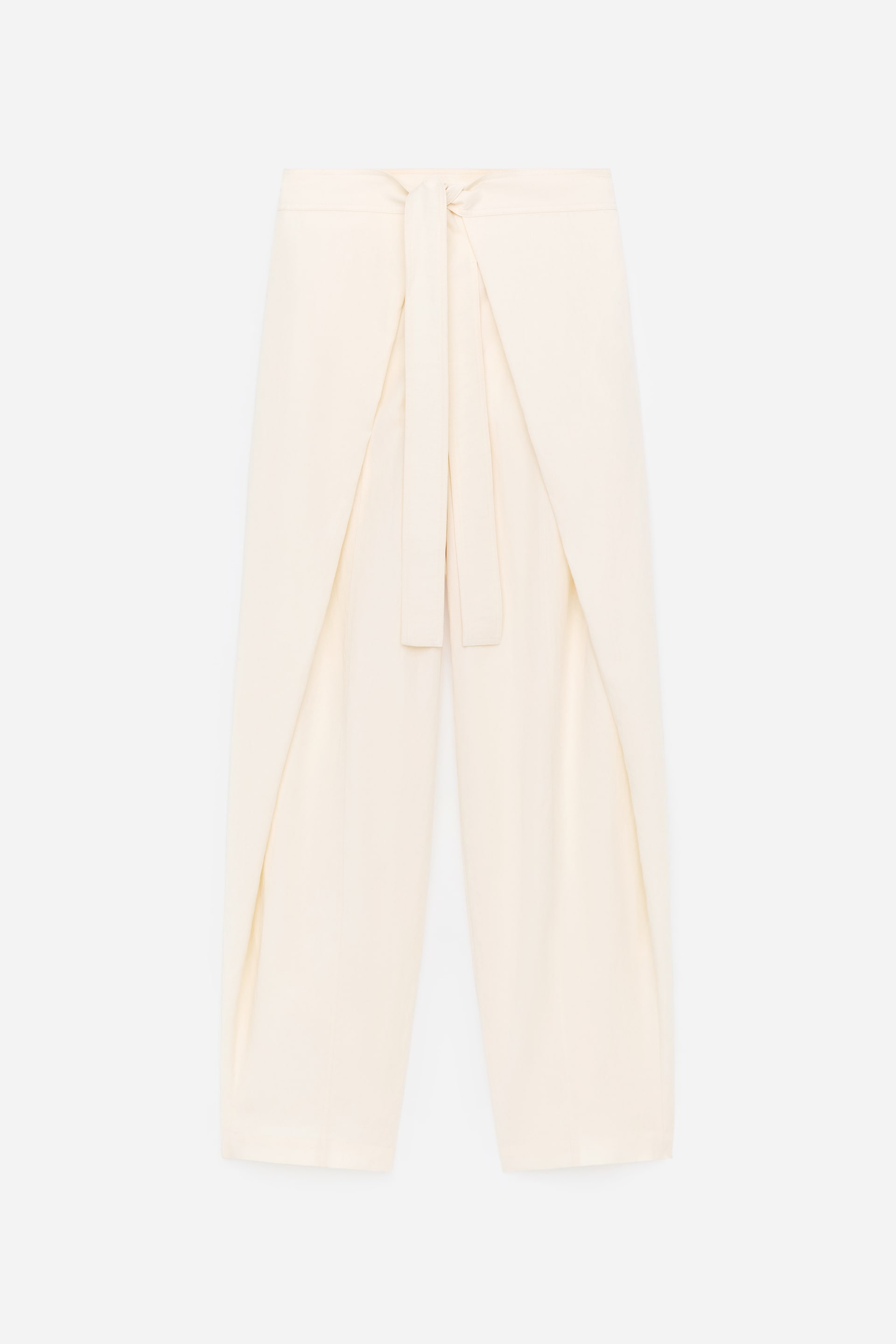 Grotere afbeelding bekijken: Deze crèmekleurige broek wordt aan de VOORKANT gepresenteerd, met een wikkelontwerp aan de voorkant en een striksluiting. De strik wordt geknoopt in de taille, waardoor een gelaagd effect over de voorkant van de benen ontstaat.