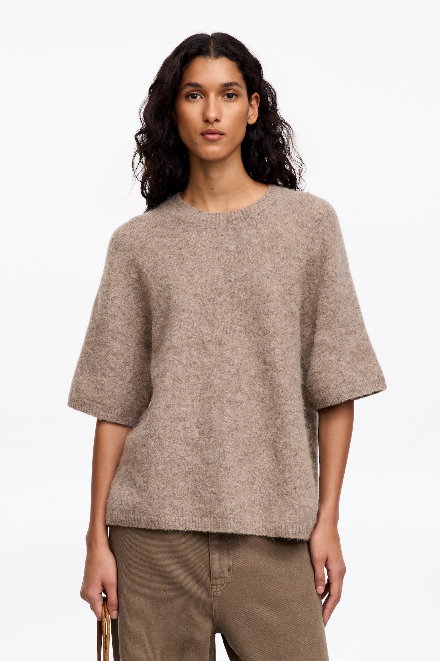 Un pull à manches courtes est présenté de face, affichant un tricot chiné brun clair à texture douce. Il est doté d'un col rond classique, de manches courtes et d'une coupe ample, et est agrémenté de finitions en maille côtelée au niveau de l'encolure, des ouvertures des manches et de l'ourlet. - 1