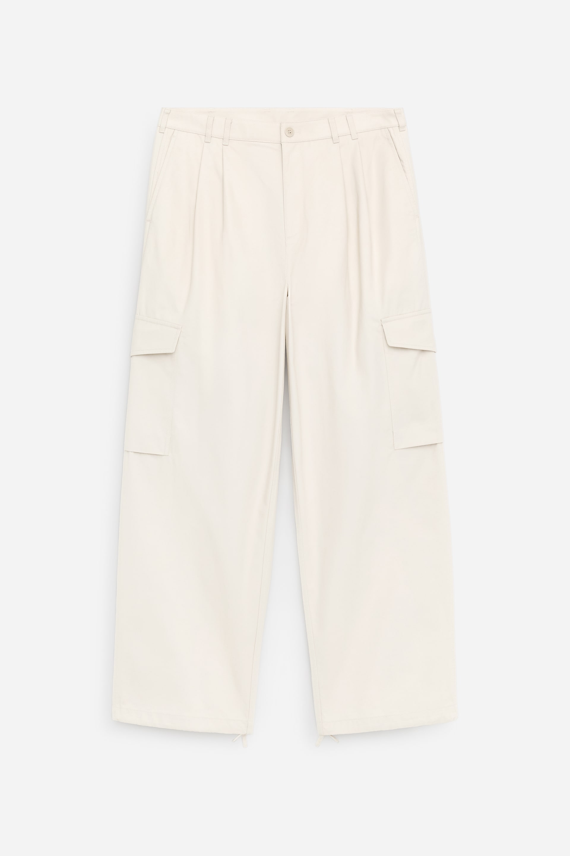 View larger image: The product is a pair of cream‑coloured, loose‑fit trousers, shown from the front, featuring a button closure, deep pleats, slanted front pockets, and belt loops. Each leg features a patch pocket with a flap, and drawstrings emerge from the bottom hems.