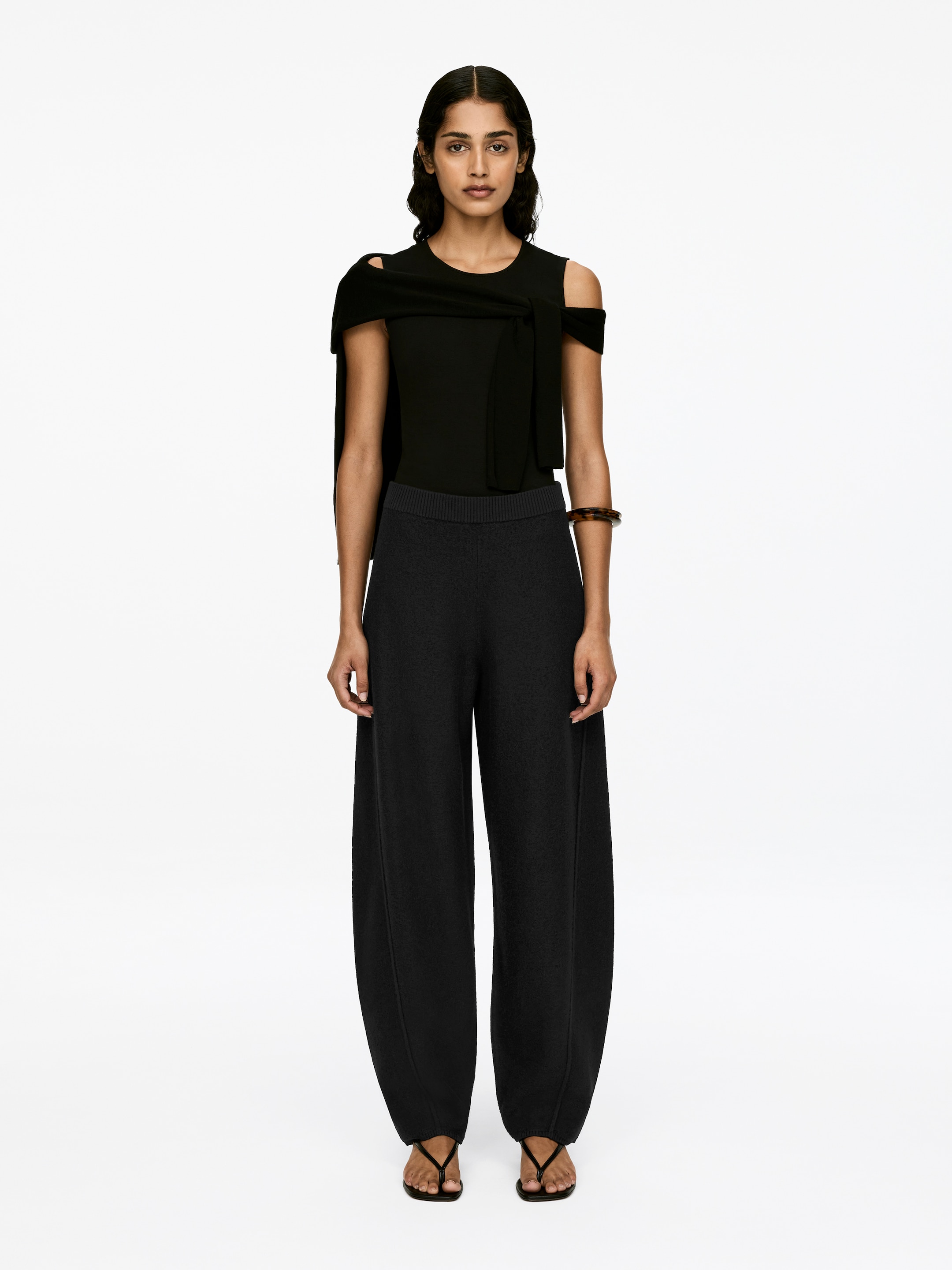 Visualizza immagine più grande: Pantaloni conici grigio scuro, realizzati in lana cotta, sono indossati dalla modella. I pantaloni presentano una fascia elastica in vita, una vestibilità ampia con una forma leggermente voluminoso, e cuciture verticali visibili su ciascuna gamba.