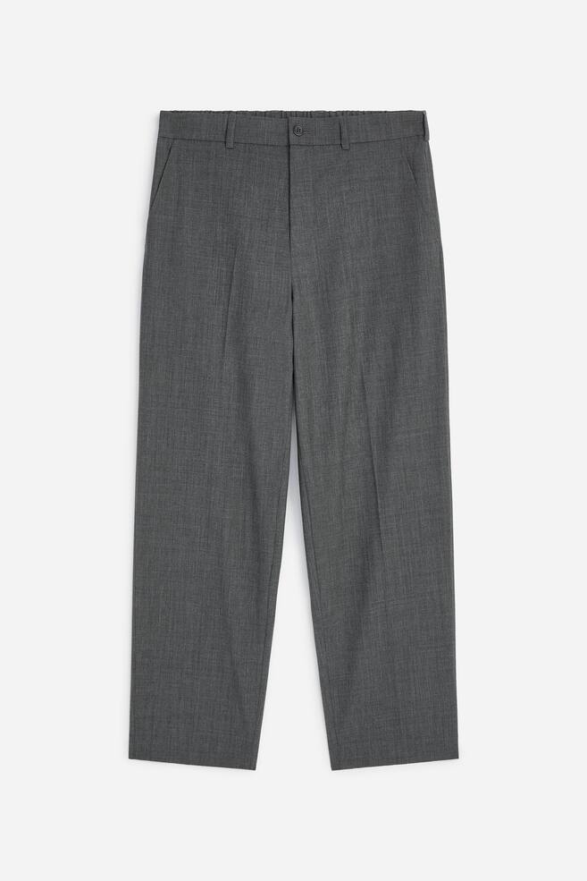Grey trousers are shown from the front, featuring a partially elasticated waistband with a button fastening and front side pockets. Prominent creases run down each leg, ending in a straight hem. - 1