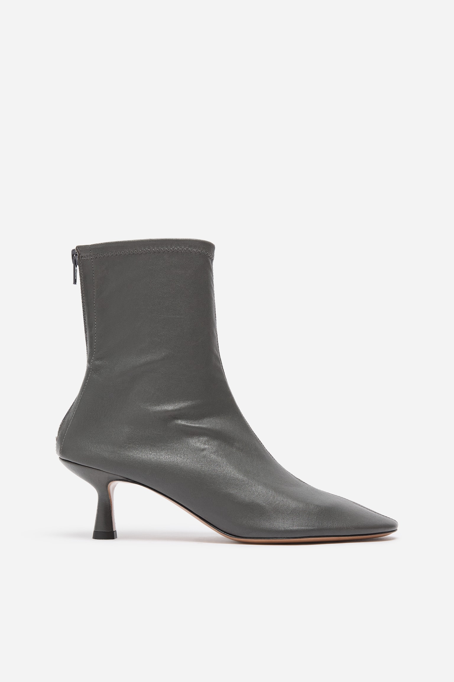 Une bottine chaussette en cuir gris foncÃ© est prÃ©sentÃ©e de profil droit, avec une silhouette Ã©purÃ©e, un bout lÃ©gÃ¨rement arrondi et un talon moyen sculptural. La bottine est conÃ§ue avec une tige ajustÃ©e, faÃ§on chaussette, et une fermeture zippÃ©e visible Ã  lâarriÃ¨re.