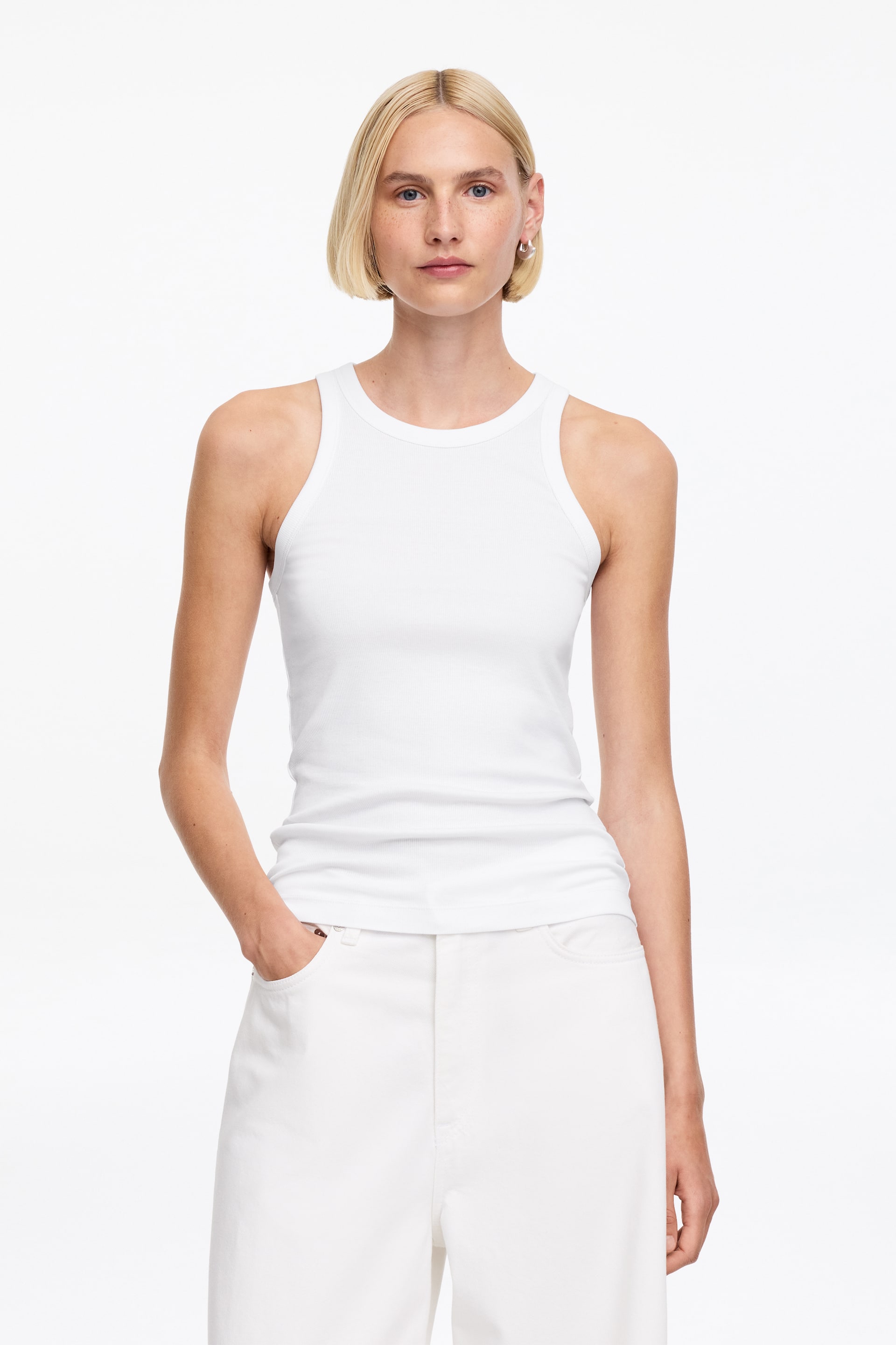 Größeres Bild ansehen: Ein weißes geripptes Tanktop wird von vorne präsentiert. Es verfügt über einen Rundhalsausschnitt und breite Träger und sitzt eng anliegend.