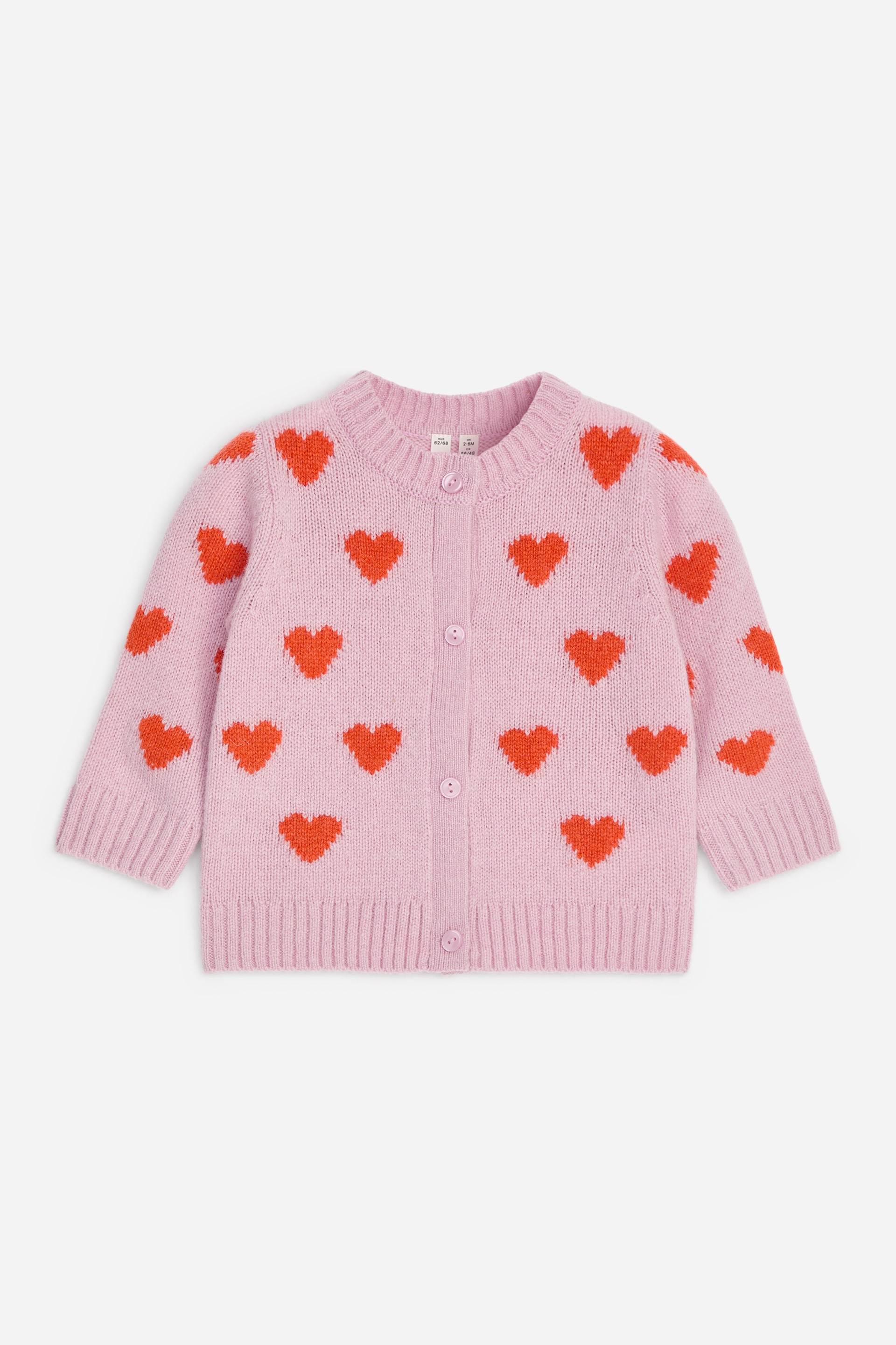 Visualizza immagine più grande: Un cardigan in lana rosa chiaro è mostrato frontalmente, caratterizzato da un motivo intarsiato a maglia con cuori rossi all-over. Presenta uno scollo rotondo, chiusura frontale con bottoni rosa coordinati e bordi a coste lungo colletto, polsini e orlo.