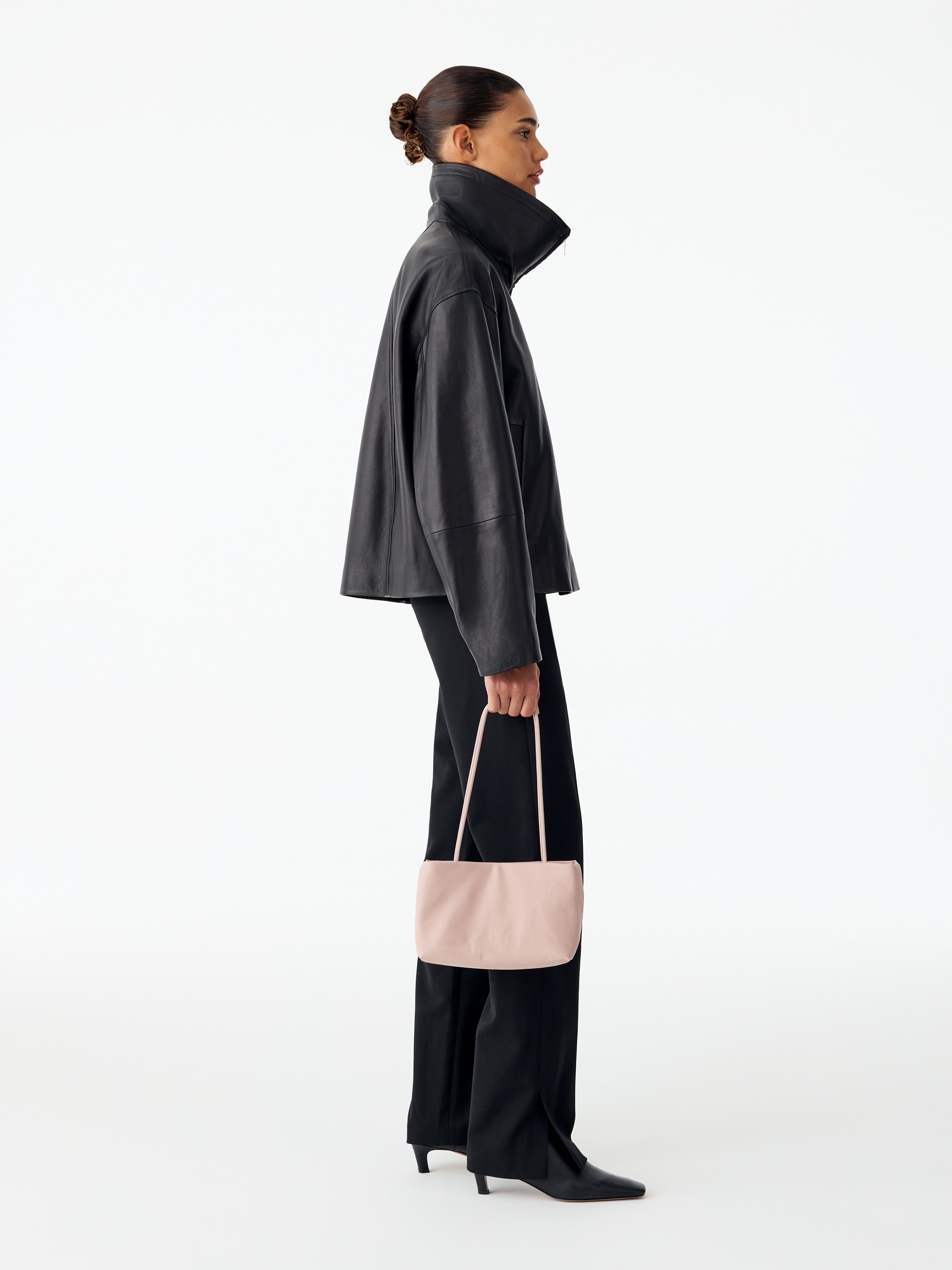 Egy világos rózsaszín nylon tote bag függőlegesen áll, elölről látható a formázott, téglalap alakú teste és sima külső felülete. Két karcsú, megnyújtott, párnázott vállpánt emelkedik felfelé a felső peremről.