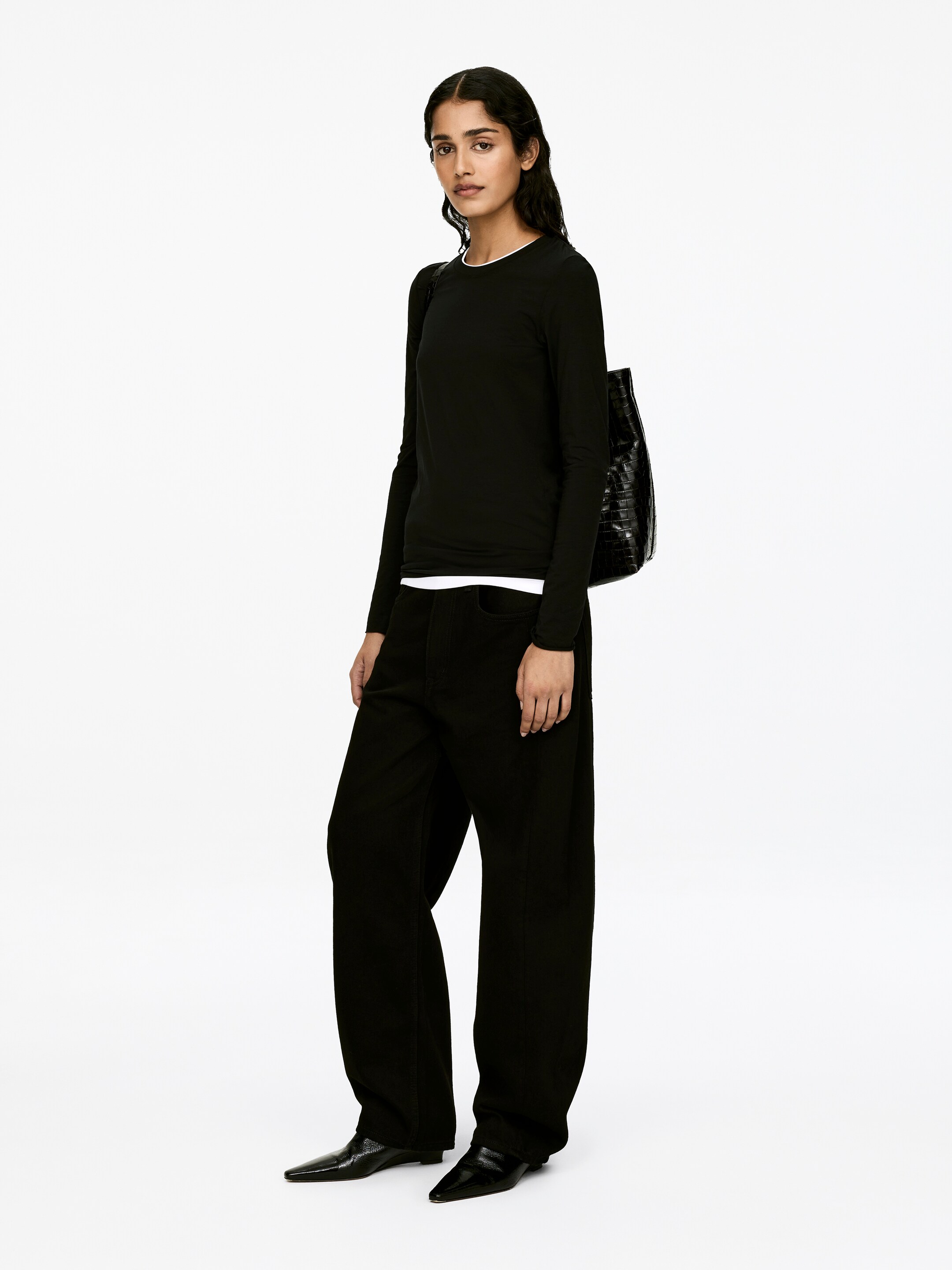 View larger image: A black long-sleeved top with a round neck is being worn by the model. It features raw edges at the bottom hem and sleeve ends, and is layered over a visible white garment.
