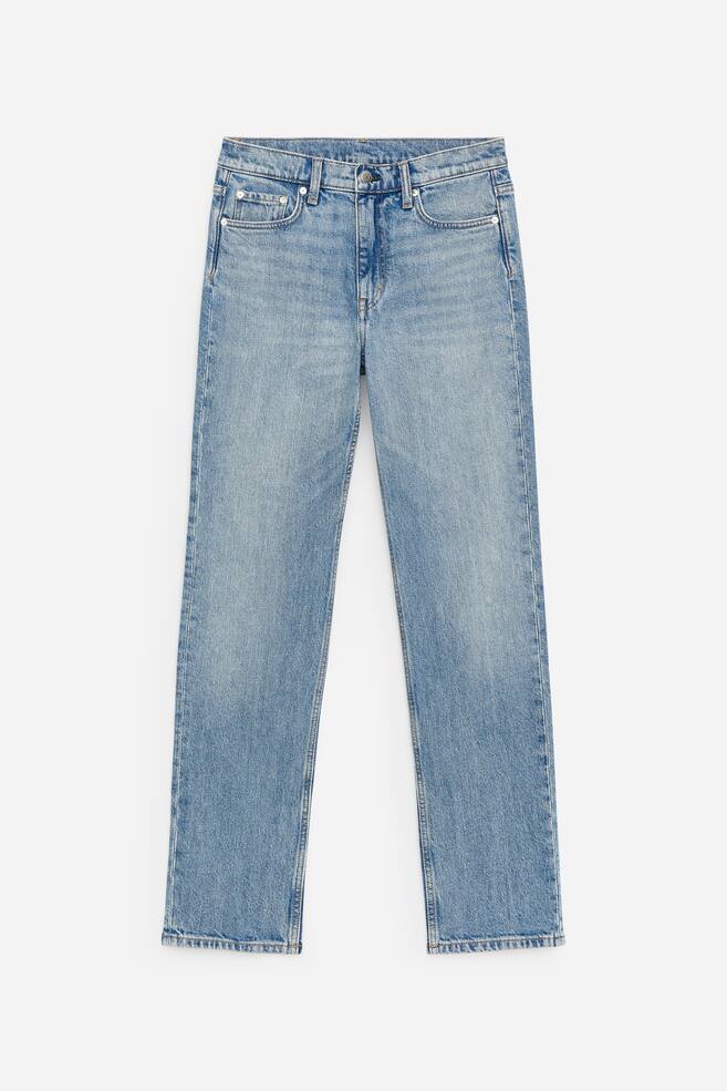 Les jeans bleu clair sont présentés de FACE, avec une taille mi-haute, une coupe ajustée et des jambes fuselées de pleine longueur. Une fermeture éclair est visible à l'avant. - 1