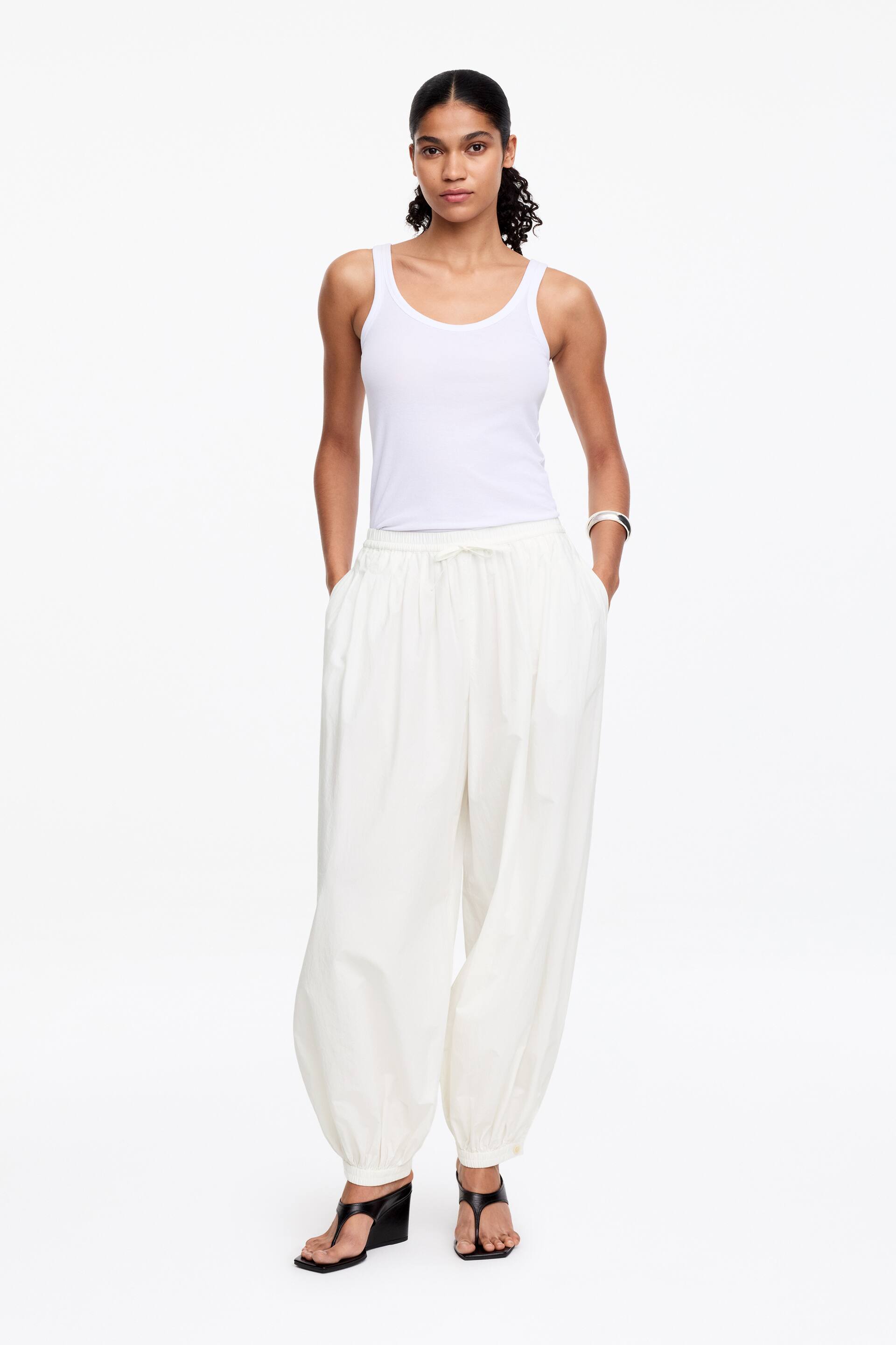 Näytä suurempi kuva: Vuorittomat housut, joissa on pallomainen siluetti, ovat mallin päällä. Niissä on joustava vyötärönauha, jossa on herkkä kiristysnauha ja pehmeät laskokset, jotka muuttuvat laskoksiksi vyötärön ympärillä. Mallin kädet lepäävät sivusaumataskuissa.