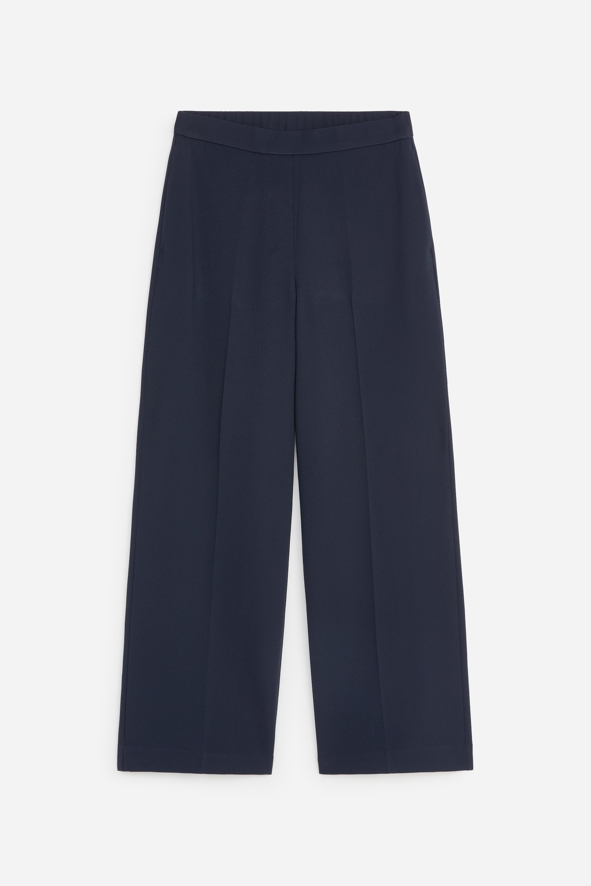 Agrandir l'image: Un pantalon large bleu foncé est présenté de face. Il présente des plis marqués au fer courant le long de l’avant de chaque jambe, et une taille plate et lisse forme le bord supérieur.