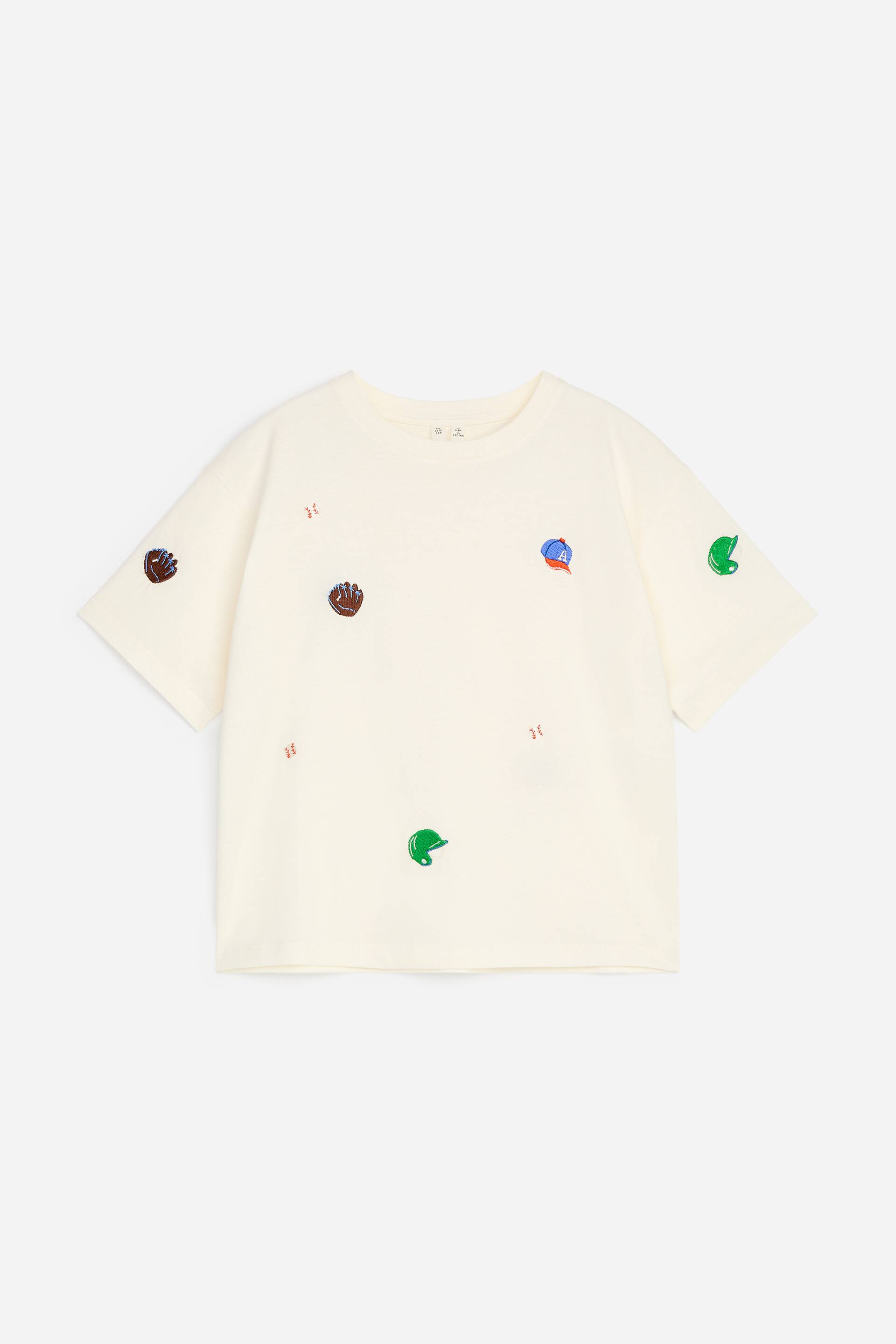 Größeres Bild ansehen: Ein locker sitzendes T-Shirt wird von vorne gezeigt und präsentiert eine cremefarbene Farbe sowie einen gerippten Rundhalsausschnitt. Es ist mit einem durchgehenden, gestickten Muster aus kleinen, bunten Baseballhandschuhen, -kappen, -helmen und -nähten versehen.