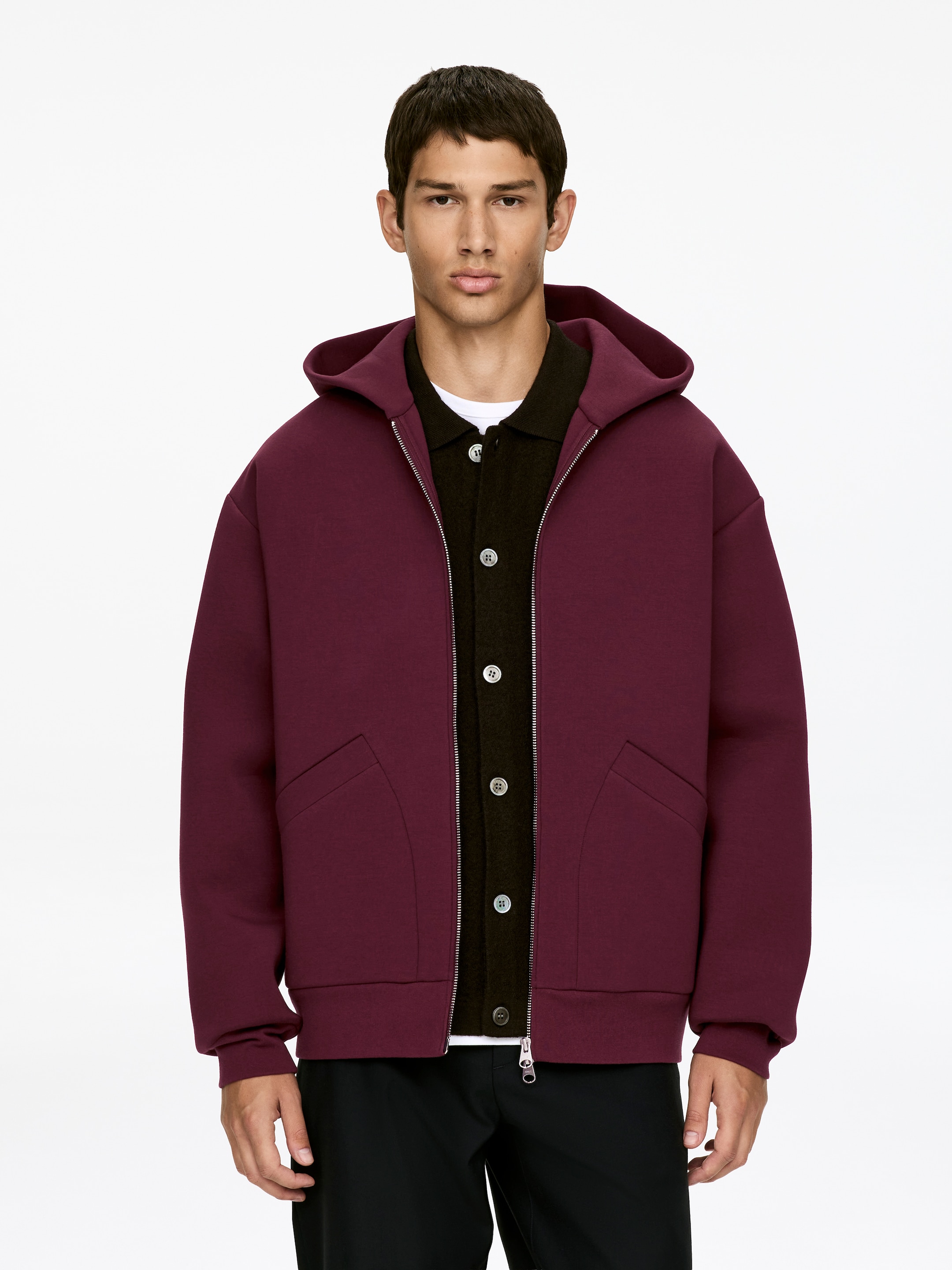Ver imagen más grande: Una chaqueta con capucha color burdeos se presenta de frente, desabrochada para revelar un cárdigan oscuro y una camiseta blanca debajo. Presenta una cremallera plateada de longitud completa, mangas largas con puños acanalados, un dobladillo acanalado y dos bolsillos delanteros inclinados.