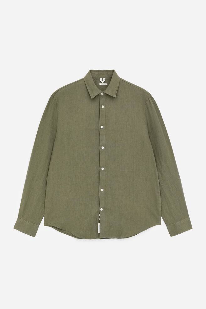 An olive green shirt is showcased from the front, featuring a textured fabric. It is designed with a pointed collar, a full-length front placket with white buttons, long sleeves, and buttoned cuffs. - 1