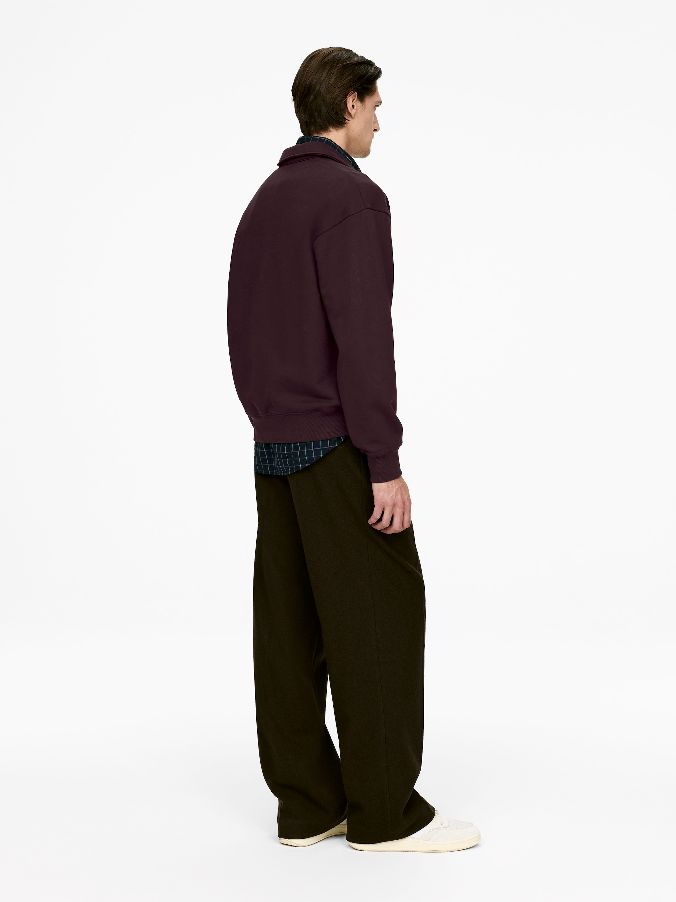Agrandir l'image: Un sweat à col en prune foncé est présenté en vue de profil droit, superposé à une chemise à carreaux foncés, avec un pantalon large et sombre tombant jusqu'aux chevilles.