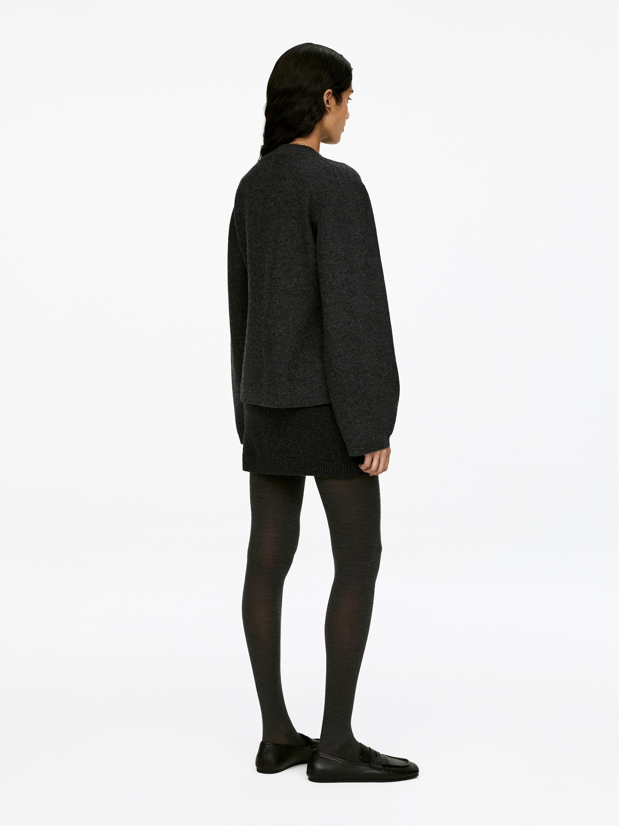 Visualizza immagine più grande: Un maglione di lana bollita grigio scuro, caratterizzato da uno stile a girocollo, maniche ampie e vita aderente, è indossato dalla modella. È stratificato sopra una gonna lavorata a maglia grigio scuro.