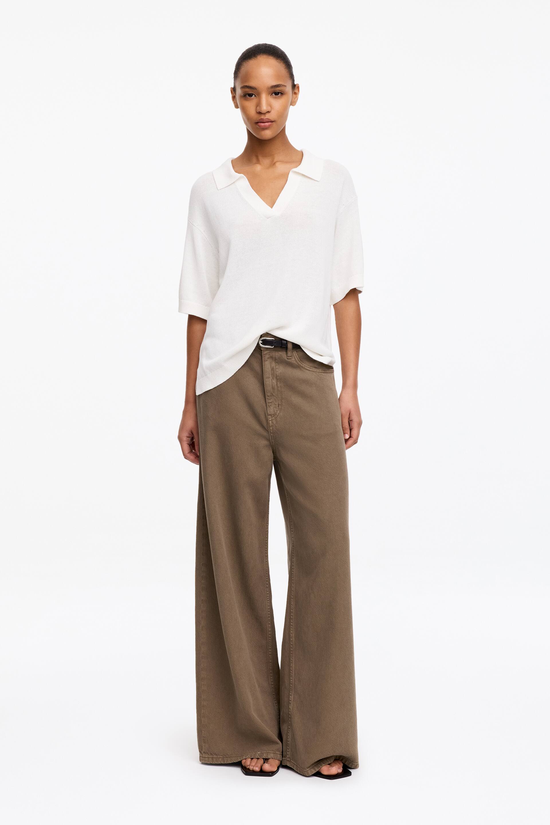 Grösseres Bild ansehen: Das Model steht und trägt eine braune, knöchellange Hose mit weitem Bein, mittlerer Bundhöhe und normaler Passform. Ein schwarzer Gürtel ist durch die Gürtelschlaufen der Hose gezogen.