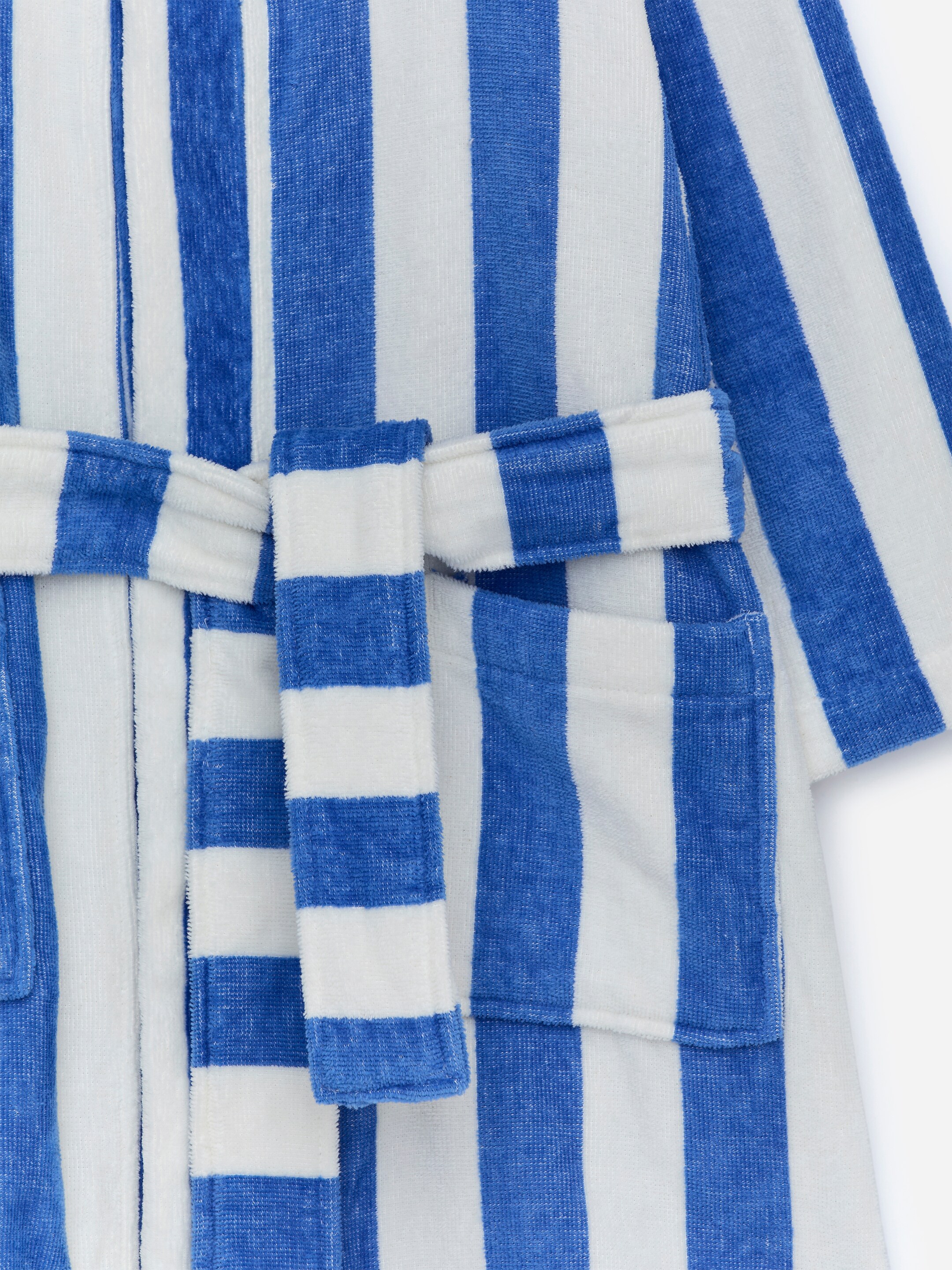 View larger image: A cotton terry robe is displaying a blue and white vertical striped pattern on its front, featuring a textured terry surface. A tie belt is positioned around the waist and is tied in a bow at the center, with two patch pockets also visible on the lower front.