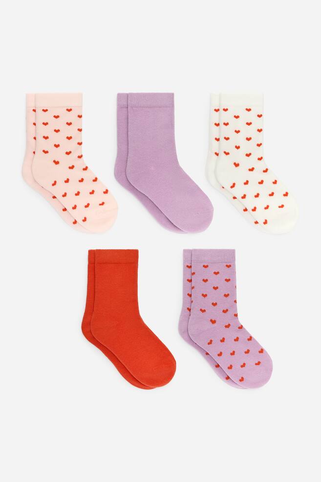 A set of five pairs of socks is arranged, each pair featuring ribbed cuffs. The set includes a light pink pair adorned with red hearts, a solid lavender pair, an off-white pair with red hearts, a solid orange-red pair, and a lavender pair with red hearts. - 1