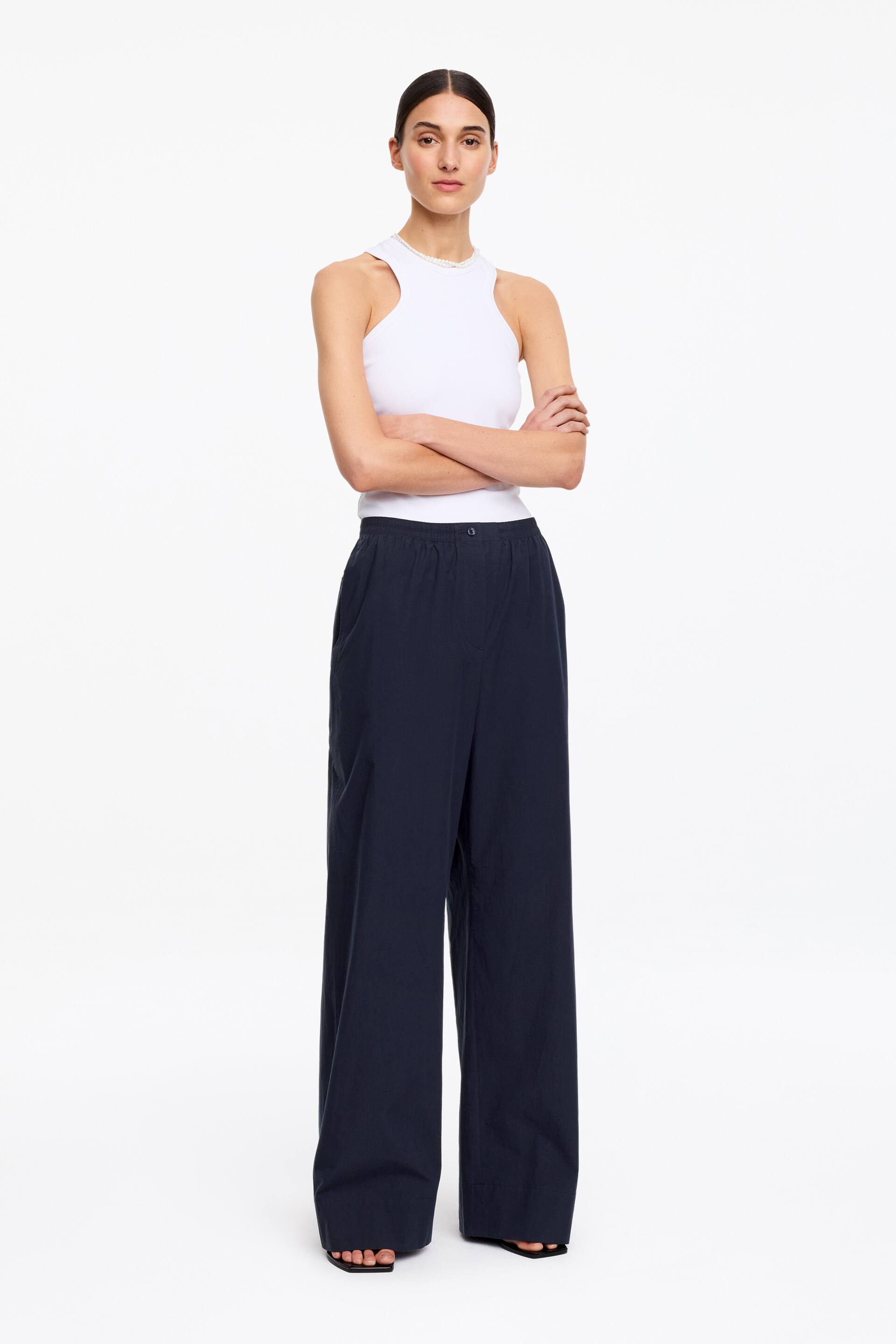 Visualizza immagine più grande: Pantaloni del pigiama blu scuro, realizzati in puro cotone, indossati dalla modella. Presentano una vita elasticizzata con chiusura a bottone, una finta patta e tasche laterali.