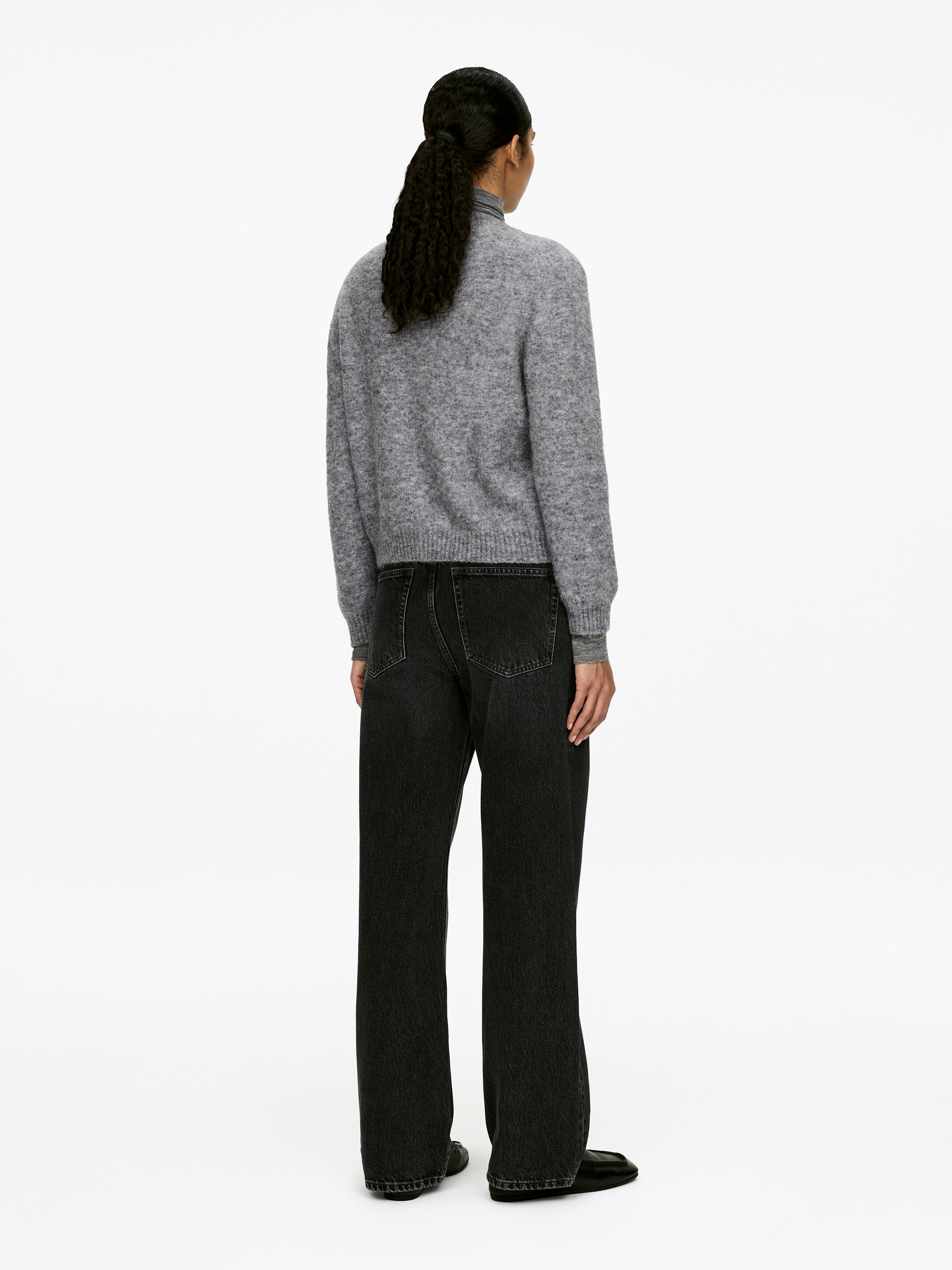 Agrandir l'image: Un pull en maille flou gris et un jean noir délavé à jambes larges sont présentés de dos. Le pull, avec un col rond, des manches longues et des poignets et ourlets côtelés, est porté par-dessus un col roulé gris. Le jean présente une coupe droite et décontractée avec des poches arrière visibles.